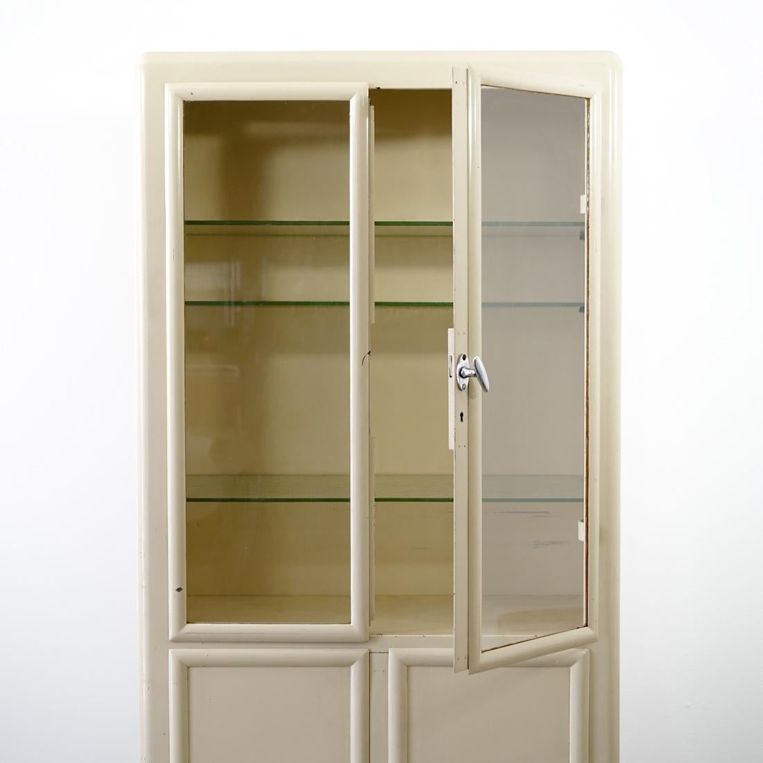 This lacquered steel medicine cabinet comes from the doctor's room of the former metalware manufacturing factory Mewa, Switzerland. 
Two glass shelves and four doors that can be opened separately, including the two upper ones in glass, allow for a