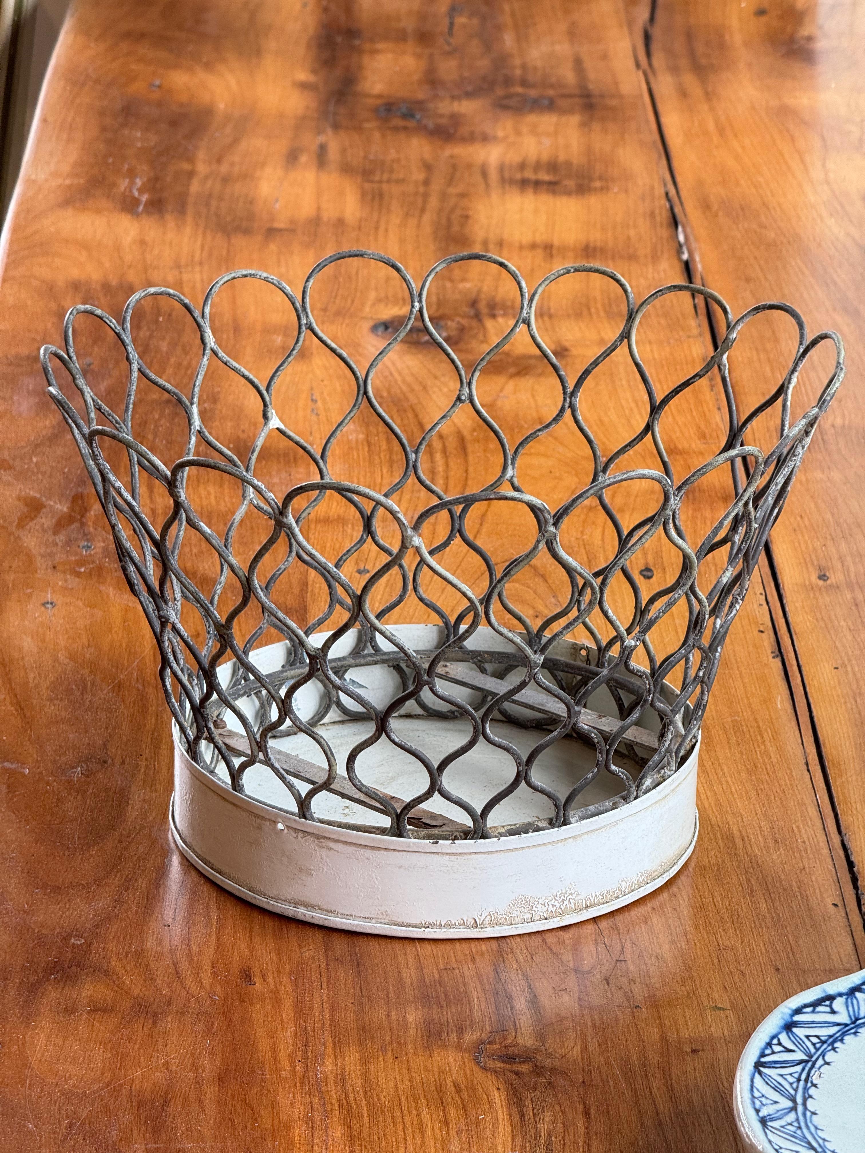 Old wire basket with looped sides and a solid metal bottom. Worn finish with a simple, sturdy look.