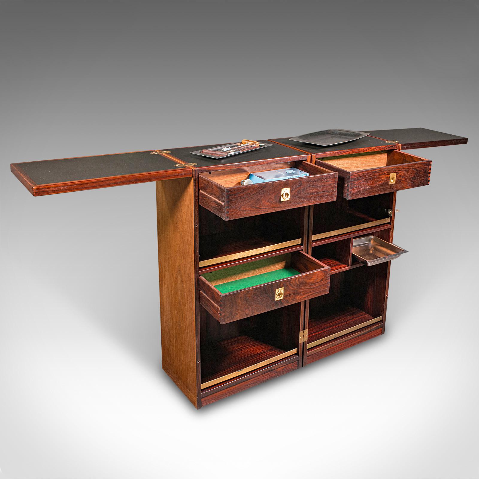 This is a vintage metamorphic cocktail cabinet. A Danish, rosewood and brass mid-century drinks bar by Reno Wahl Iversen for Dyrlund, circa 1960.

Superb mid-century modern living, with this high quality fold-out cocktail bar
Displays a desirable