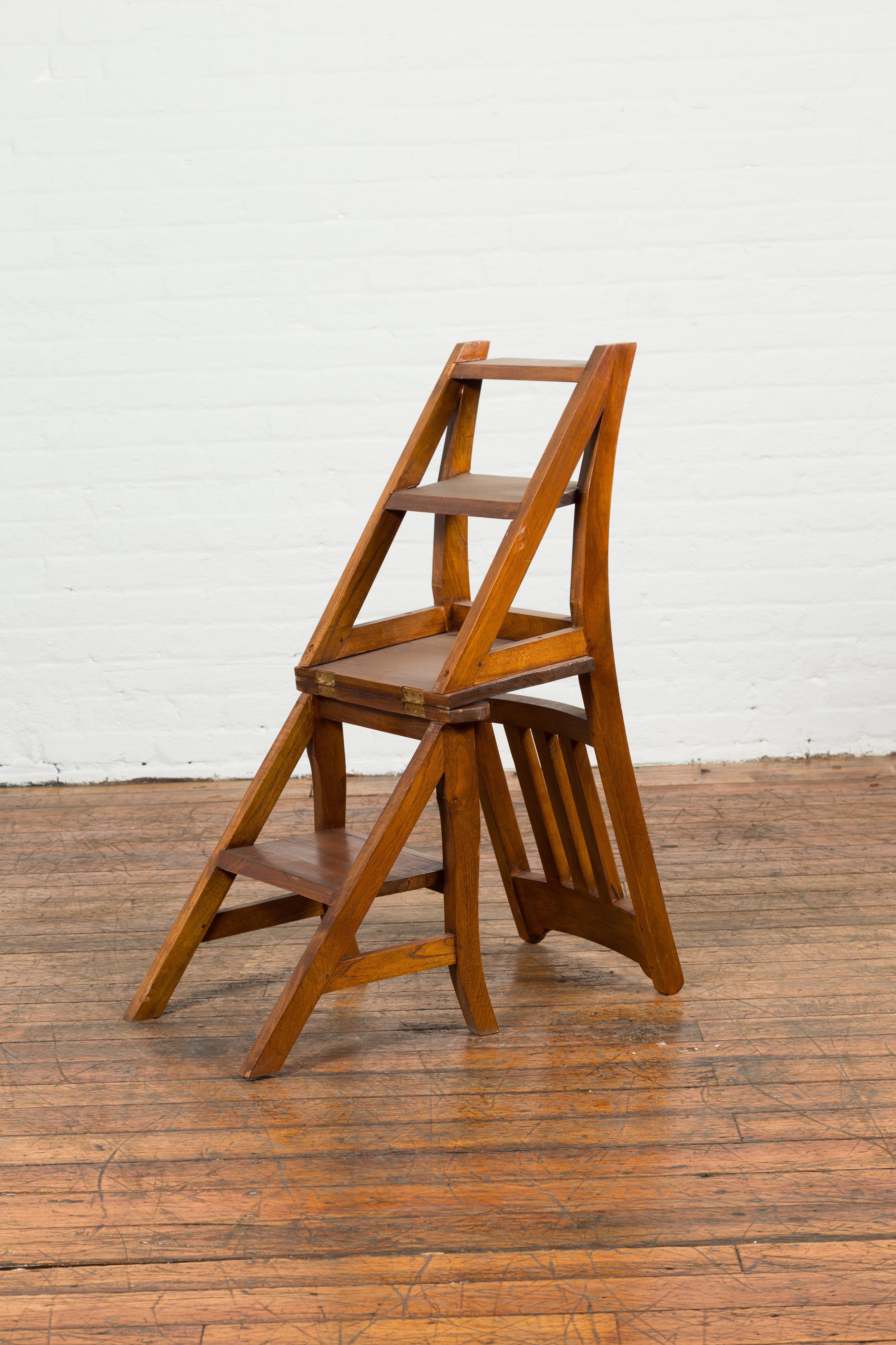 A vintage Indian metamorphic wooden ladder chair from the mid-20th century. Created in India during the midcentury period, this convenient chair features a slanted slatted back flowing into the hind legs. The lower section showcases a shelf, secured