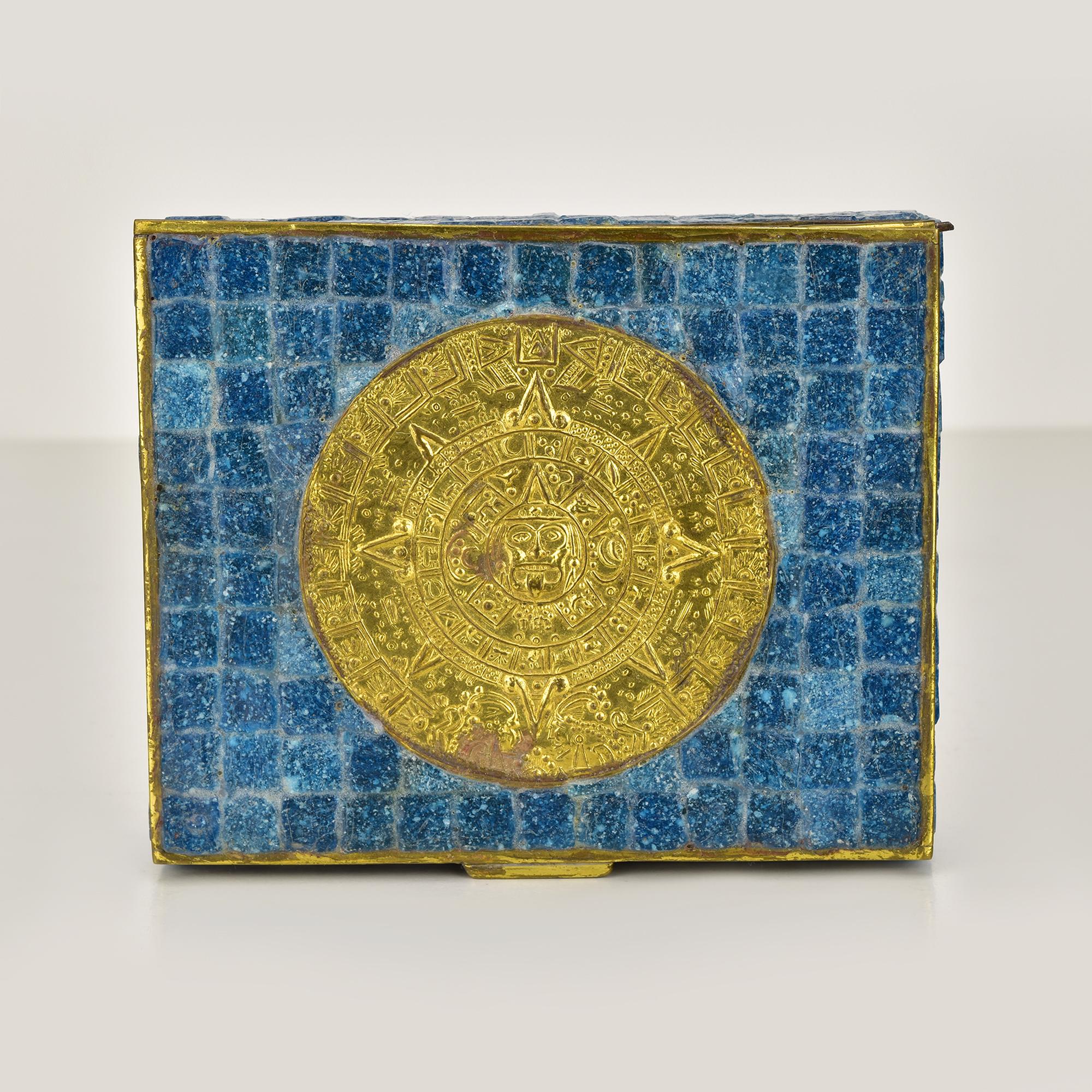 Esta singular caja vintage de México está adornada con vibrantes mosaicos de vidrio azul, que forman una cautivadora superficie texturizada. La pieza central de esta pieza es un intrincado adorno de metal dorado, que recuerda a los motivos