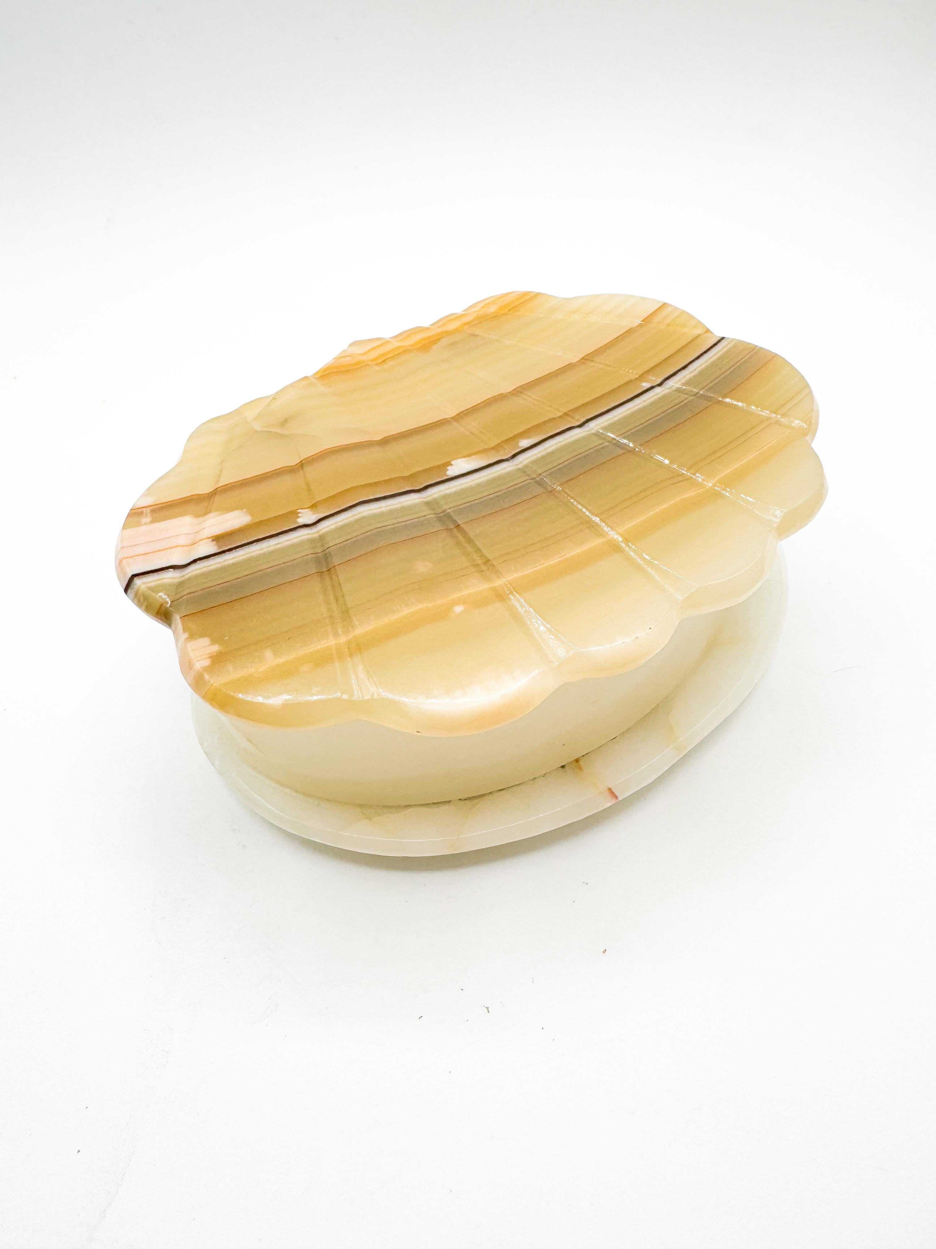 This vintage onyx trinket box features a beautifully sculpted shell-shaped lid with soft, undulating edges and natural banding in tones of caramel, sand, and cream. Hand-carved in Mexico, this piece showcases the organic beauty of onyx, with