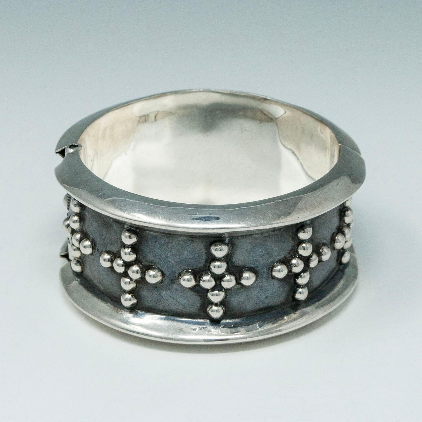 Vintage Mexican Silver Dotted Cross Clamper

A graphic silver dotted cross motif on a black background encircles this hinged clamper bracelet made in Mexico. It measures 2-3/8 inches in diameter and is 1.25 inches wide. The weight is 66 grams and it