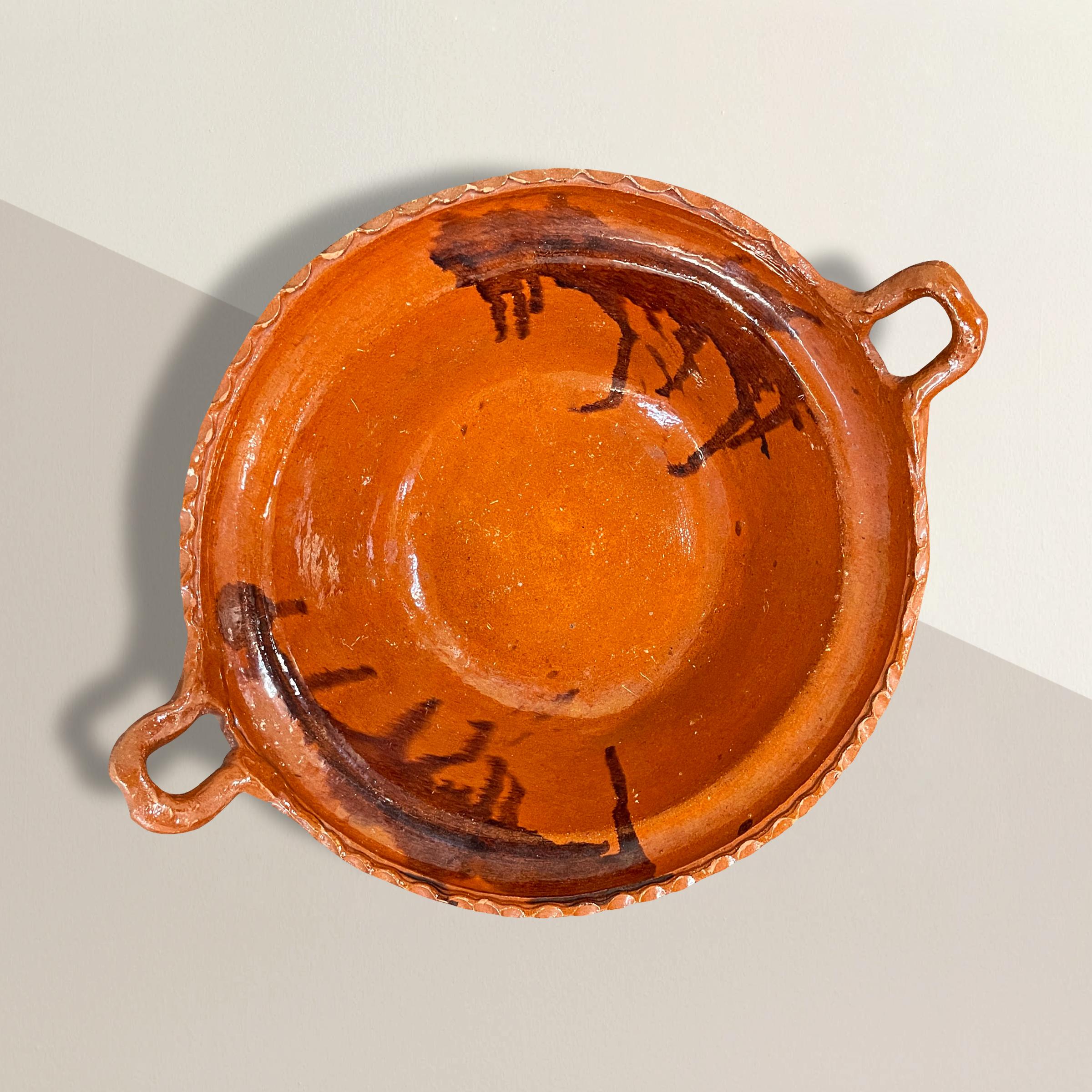 A beautiful vintage Mexican terracotta bowl with two handles, a ruffled lip, two large drip glazed splotches inside. The exterior is unglazed. Perfect for holding fruits and vegetables on your kitchen island, or ask us about having a custom mount