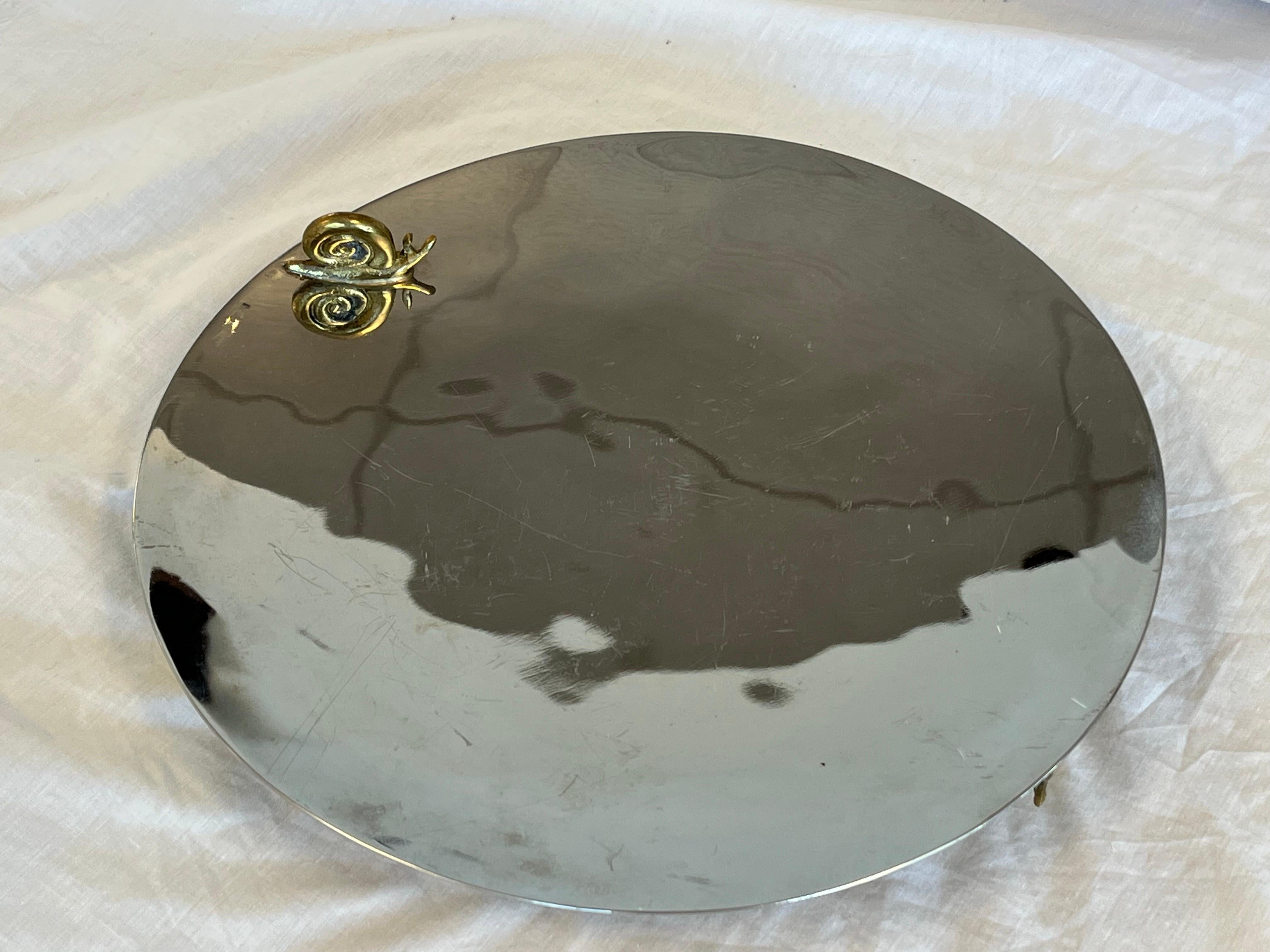 A contemporary serving tray or platter with four whimsical snail decorations, three functioning as the feet while a fourth sits atop the gorgeous tray, by skilled designer Michael Aram. Who is Michael Aram, 