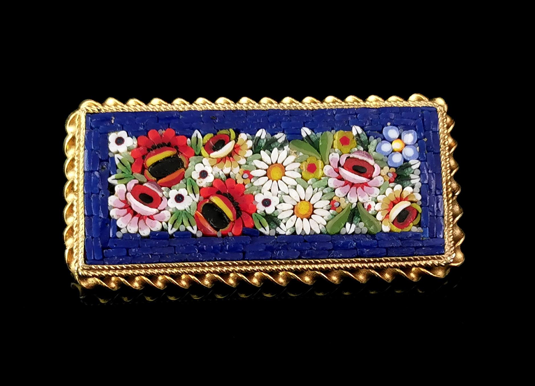 A beautiful vintage c1940s Micro Mosaic brooch.

Painstakingly created in Italy from many tiny of pieces of ceramic and laid out in a pretty floral design with a rich royal blue border.

The micro mosaic is set into a rectangular shaped gold tone