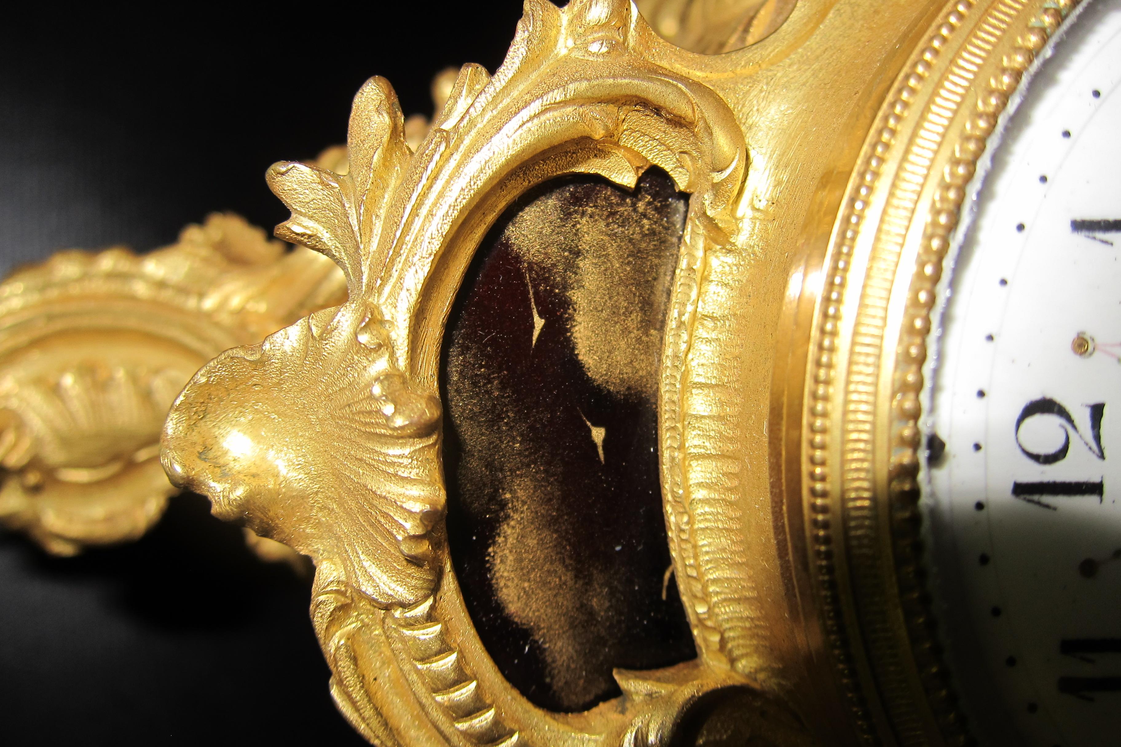 Cette horloge de boudoir française de la fin du XIXe siècle est dotée d'un cadre orné de volutes en bronze doré. Dans le cadre de ce garde-temps vintage se trouve une merveilleuse peinture en émail peinte à la main et signée d'une femme