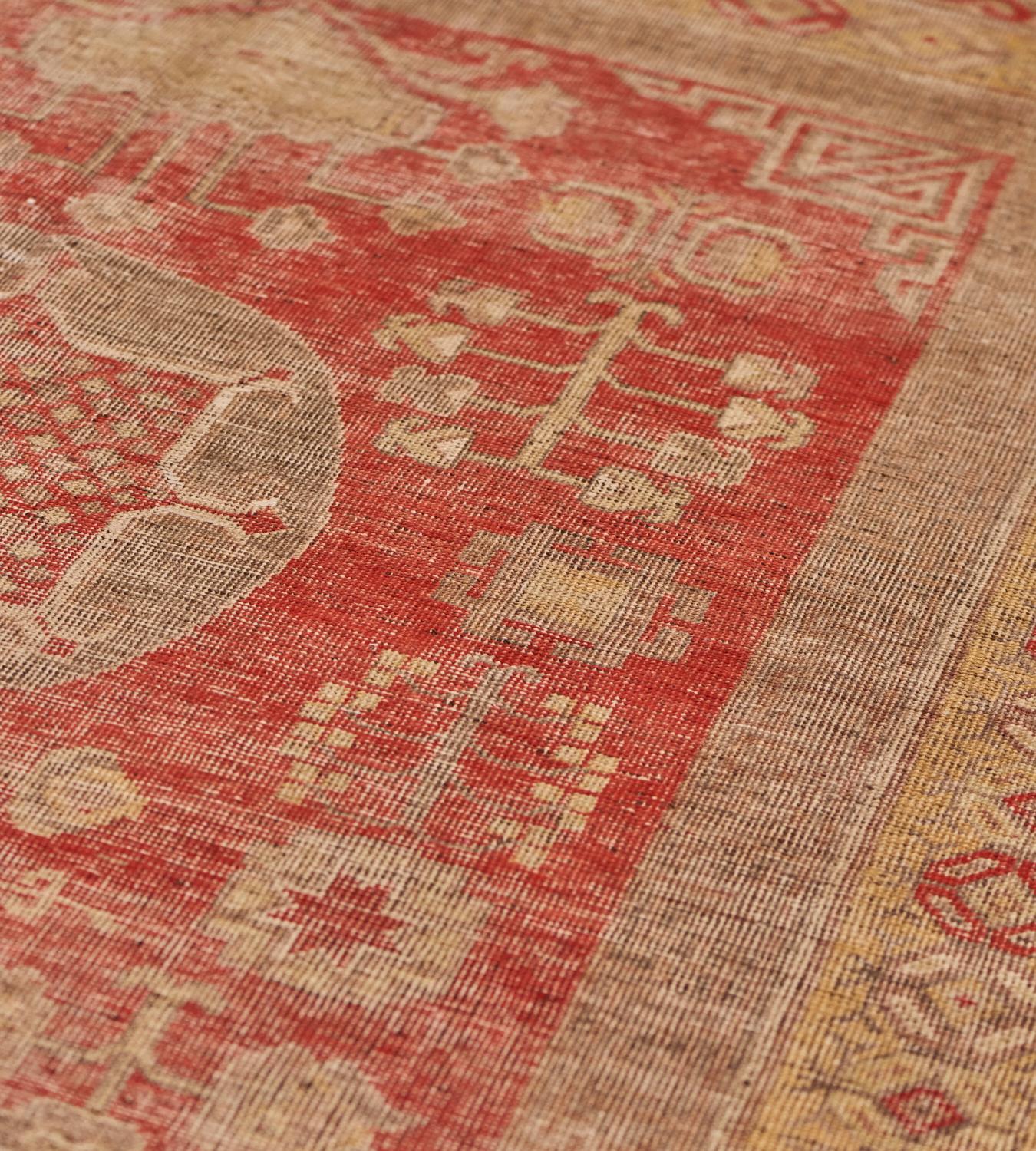 This vintage Khotan carpet has a plum red field with a central column of three shaded buff roundels the lower and upper containing a large panel, the central roundel with linked flowerheads, each panel surrounded by angular flowerheads, floral