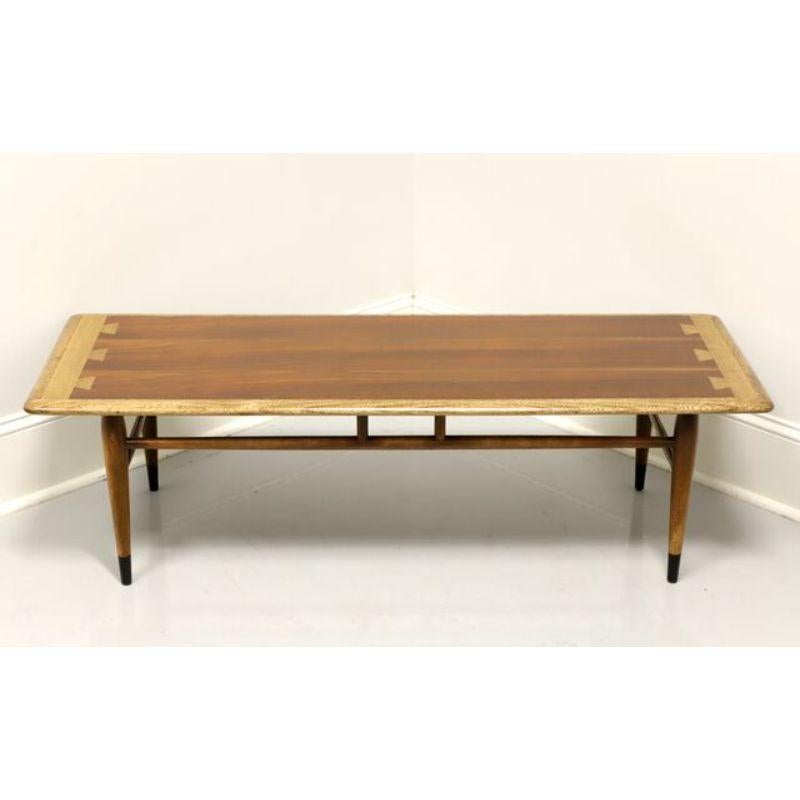 A rectangular shaped Mid Century Modern style coffee table by Lane, their Acclaim Series designed by Andre Bus. Walnut with lighter stained dovetail design to top, stretcher base, tapered round legs and black painted feet. Made in Altavista,