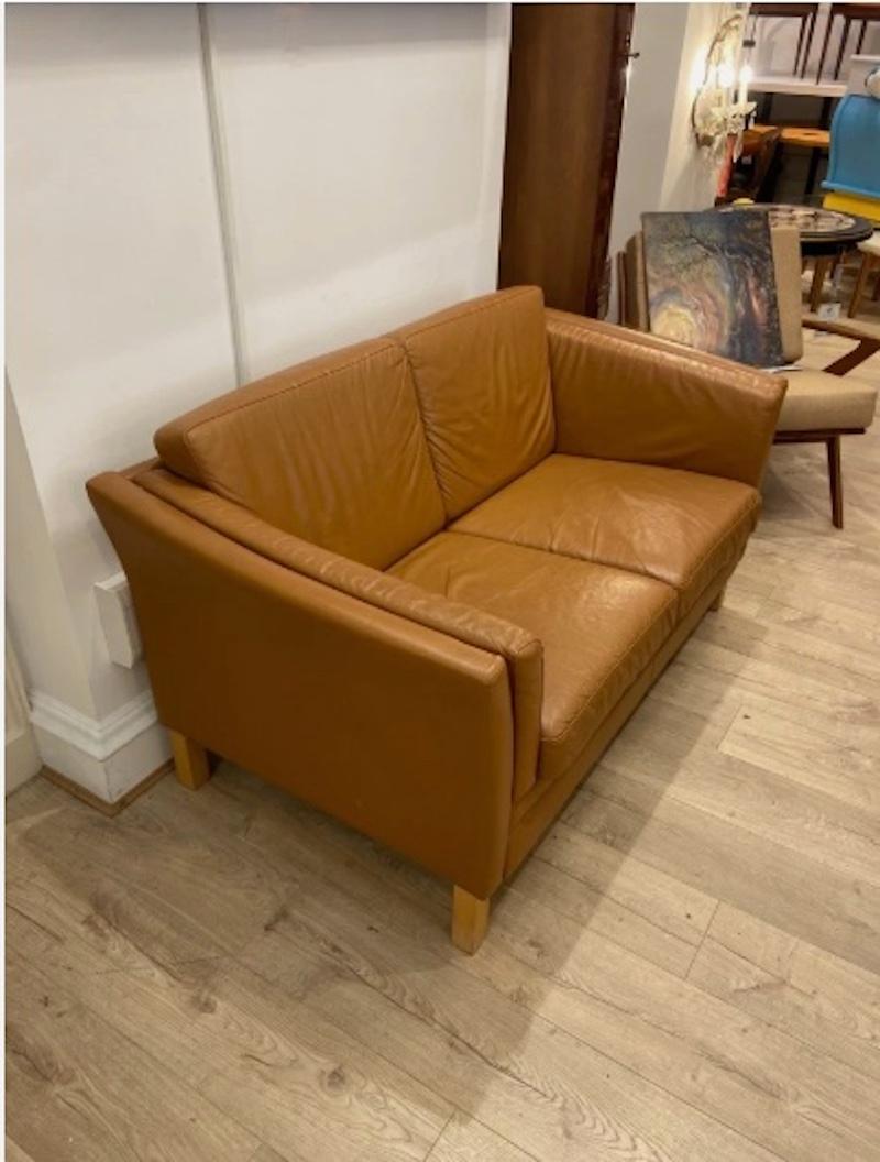 Un classico divano danese a due posti della metà del XX secolo in pelle marrone invecchiata, che offre un fascino senza tempo e un comfort quotidiano in una forma compatta e versatile. 

L'autentica patina della pelle crea un fascino rilassato e