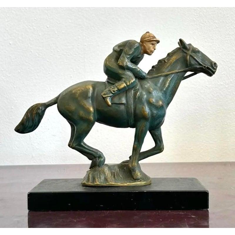 Questa scultura in metallo raffigura una figura equestre, con un cavaliere seduto in posizione eretta in cima a un cavallo che cammina con sicurezza. La postura del cavaliere e la zampa anteriore sollevata del cavallo trasmettono un senso di