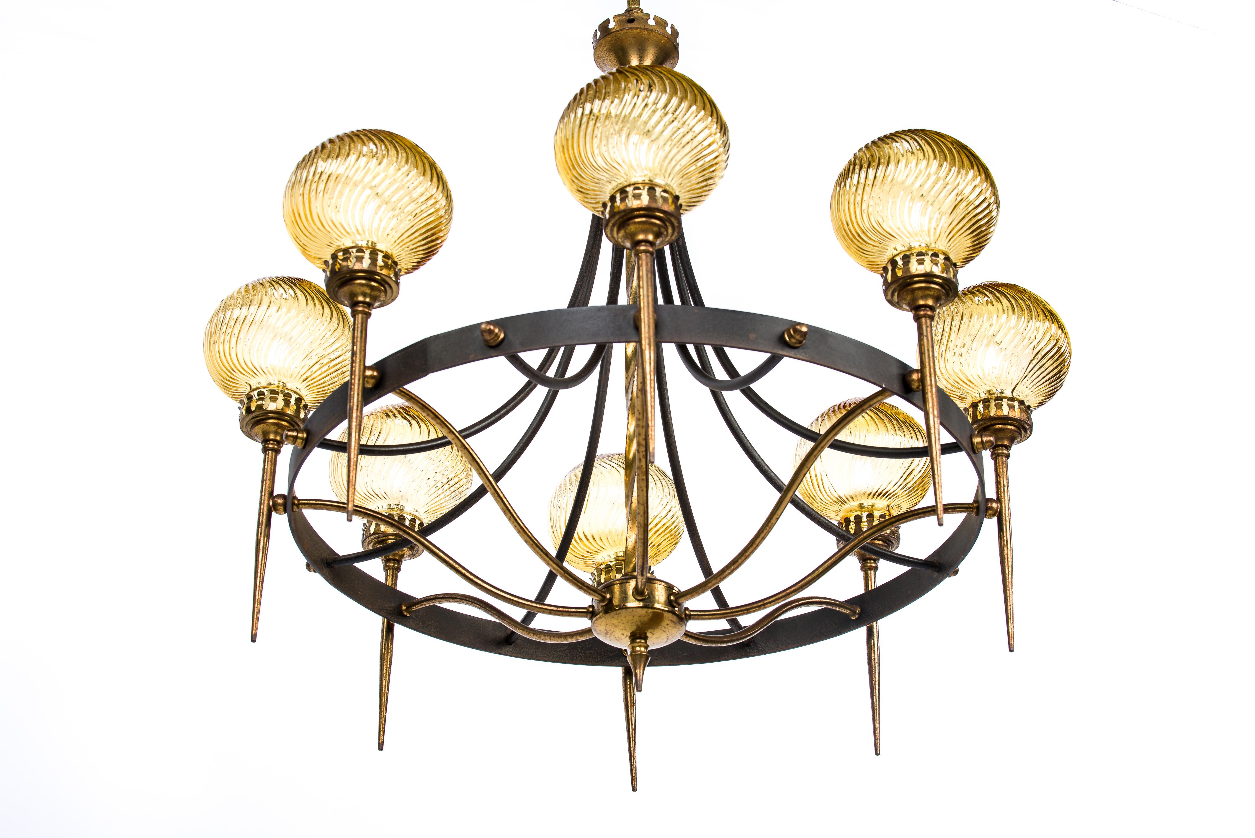 This elegant chandelier was made in France in the 1960s. It features a twisted central brass column with a black patinated steel ring supporting 8 brass torches. The torches end with beautiful yellow twisted glass covers. This one-of-a-kind