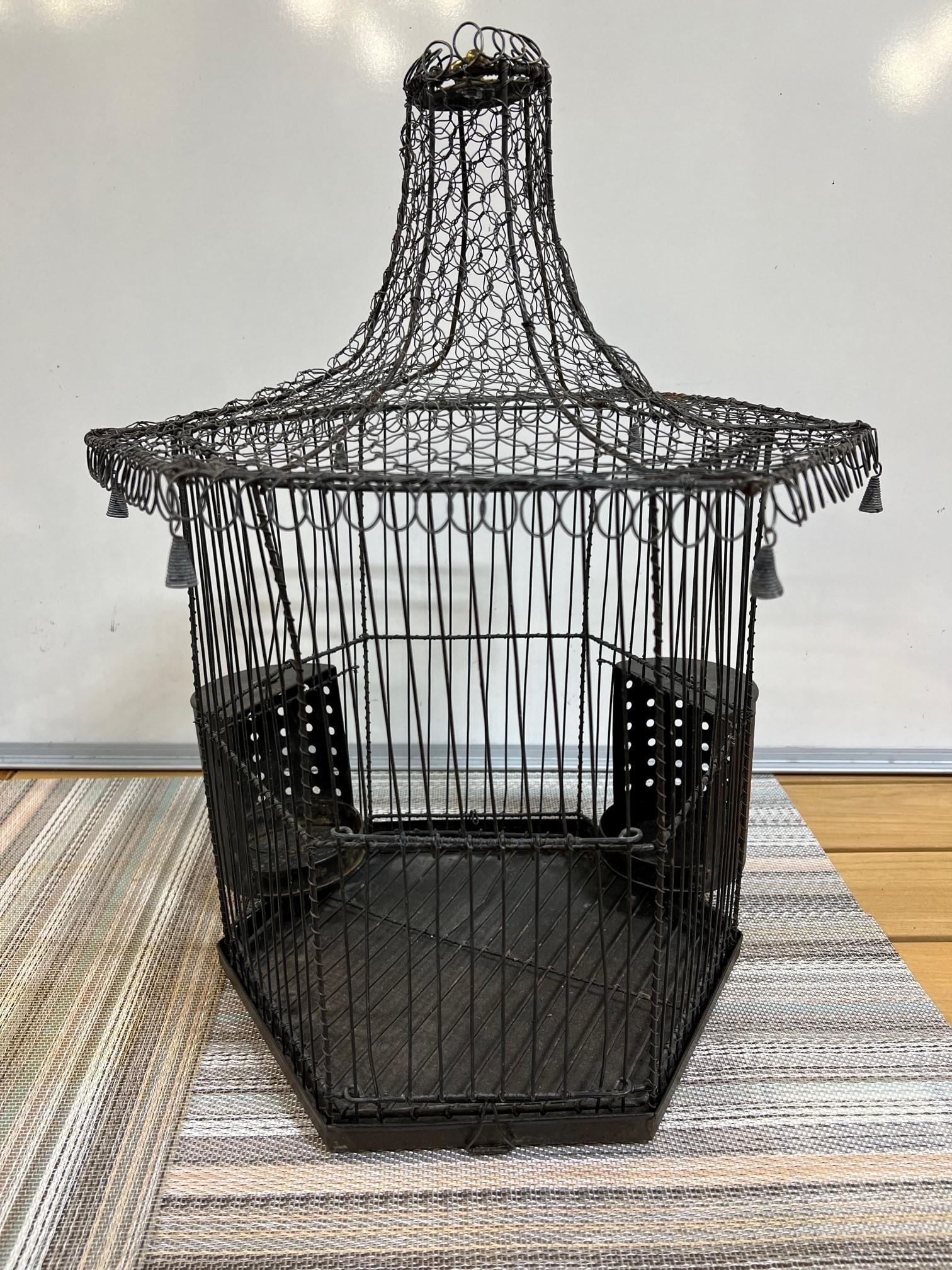 This is a nice mid-century iron and wire birdcage with hanging tassels and external protrusions for food and water. There is a door which slides up for access to the interior and two clips which hold the bottom tray. The birdcage is in good