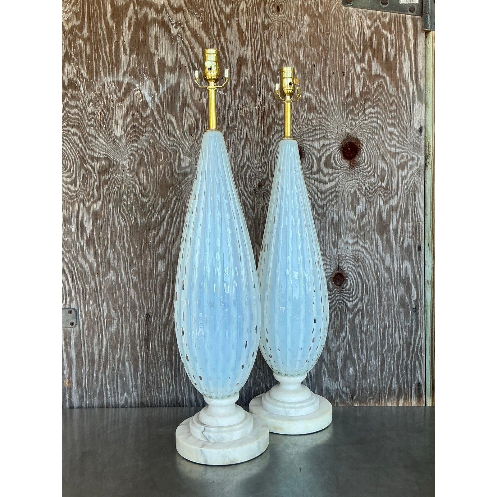 Elevate your interior with this stunning pair of mid-century modern Italian Murano glass table lamps, gracefully designed with elongated, ribbed glass bodies. Featuring a delicate swirl pattern with opalescent hues, these lamps exude timeless