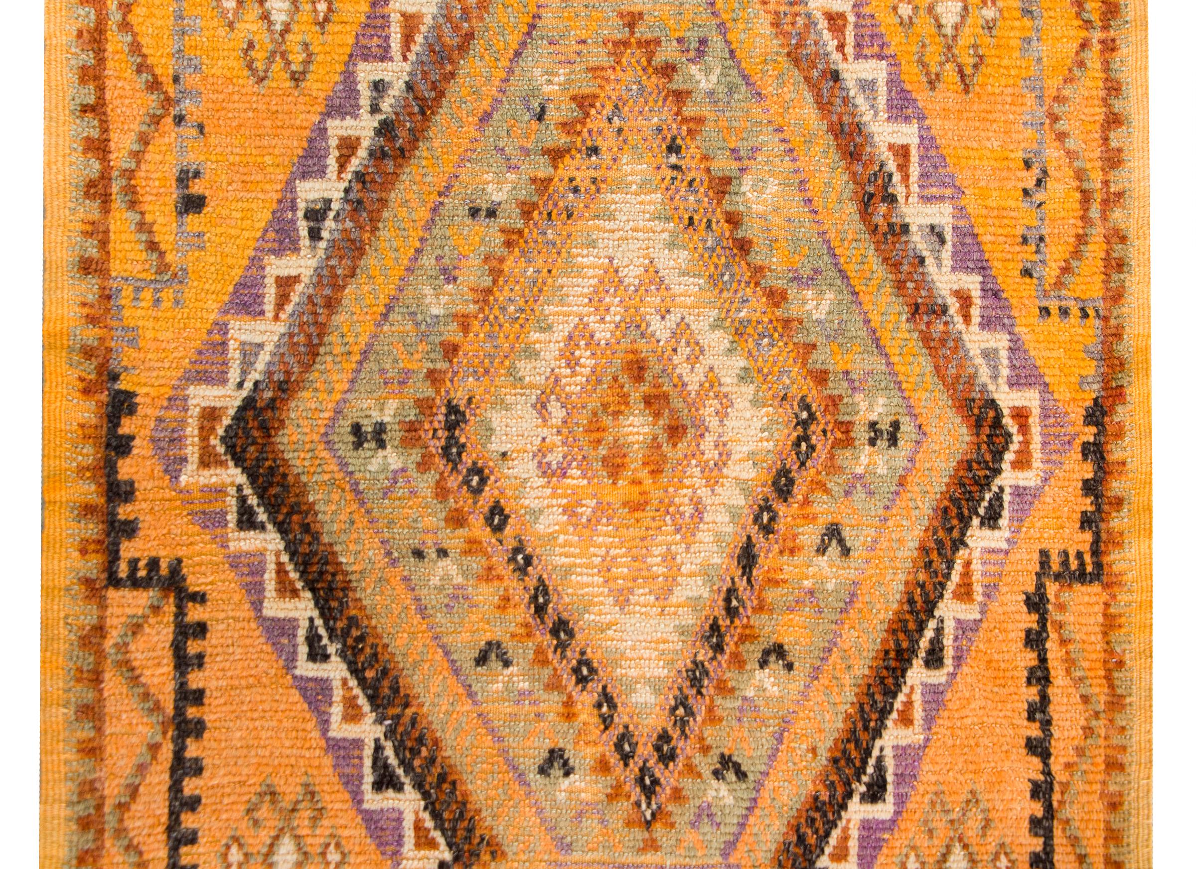 A brilliant vintage mid-20th century Moroccan rug with a central stylized floral diamond surrounded by repeated petite geometric patterned stripes woven in violet, orange, green, and gold, and all set against a saturated gold background.