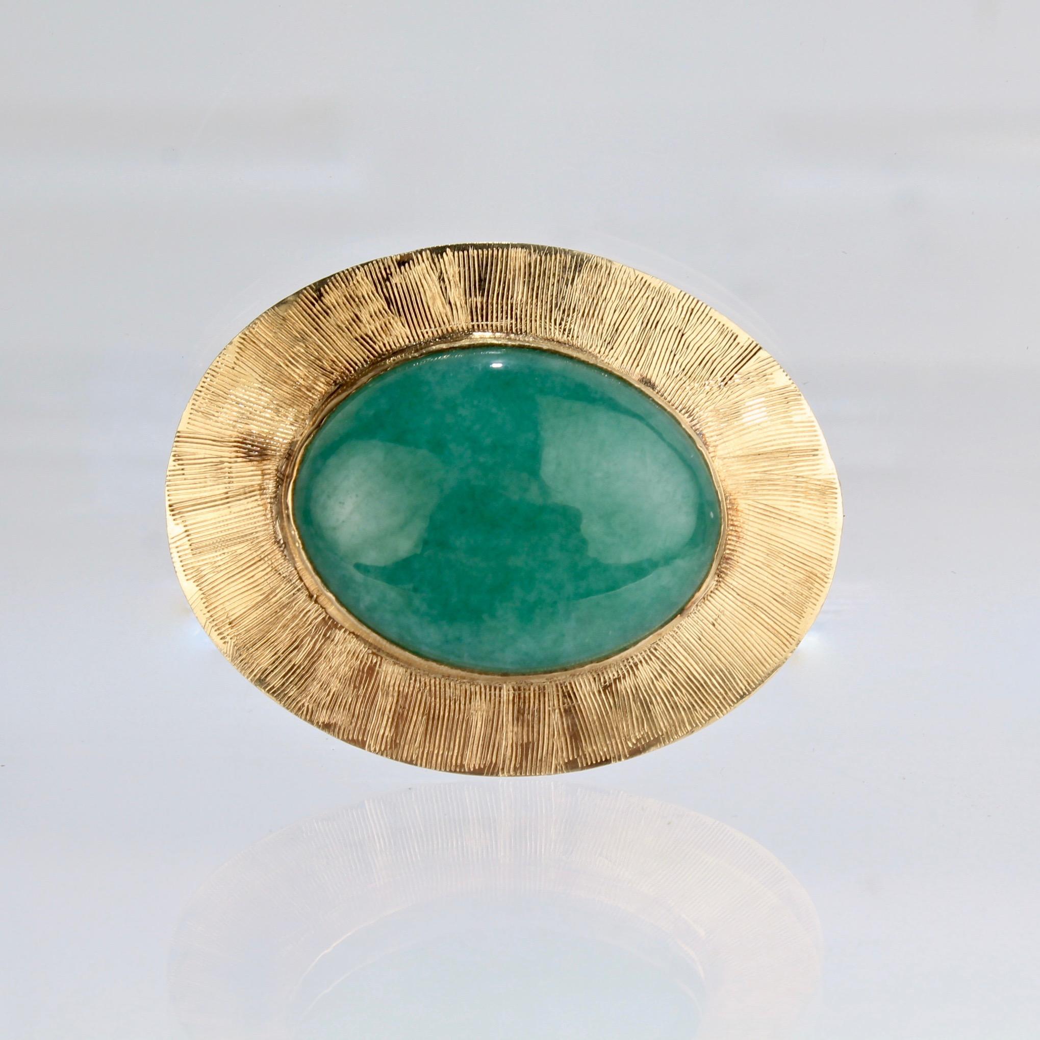 A fine vintage gold and jade brooch or pin.

With a jadeite cabochon bezel set in a textured gold setting. 

Marked to the reverse 14K for gold fineness.

Width: ca. 32 mm

Items purchased from this dealer must delight you. Purchases may be returned