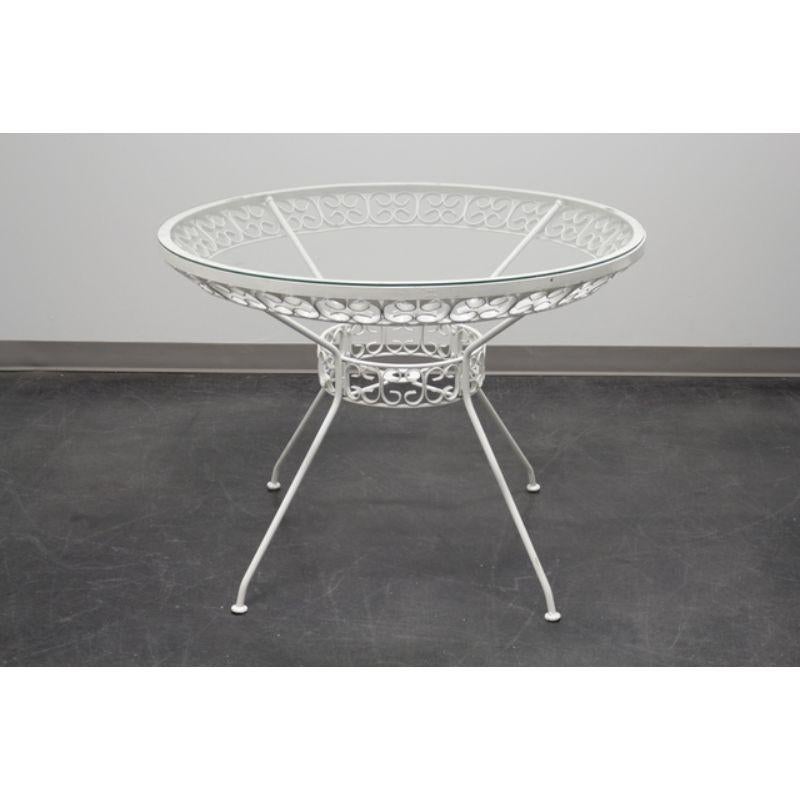 An iconic patio set designed by Arthur Umanoff. Produced by Sid Leach of Alabama in the 1950's. White painted round wrought iron table with glass top, and four white painted high-back wrought iron side chairs with vinyl cushioned seats. Made in