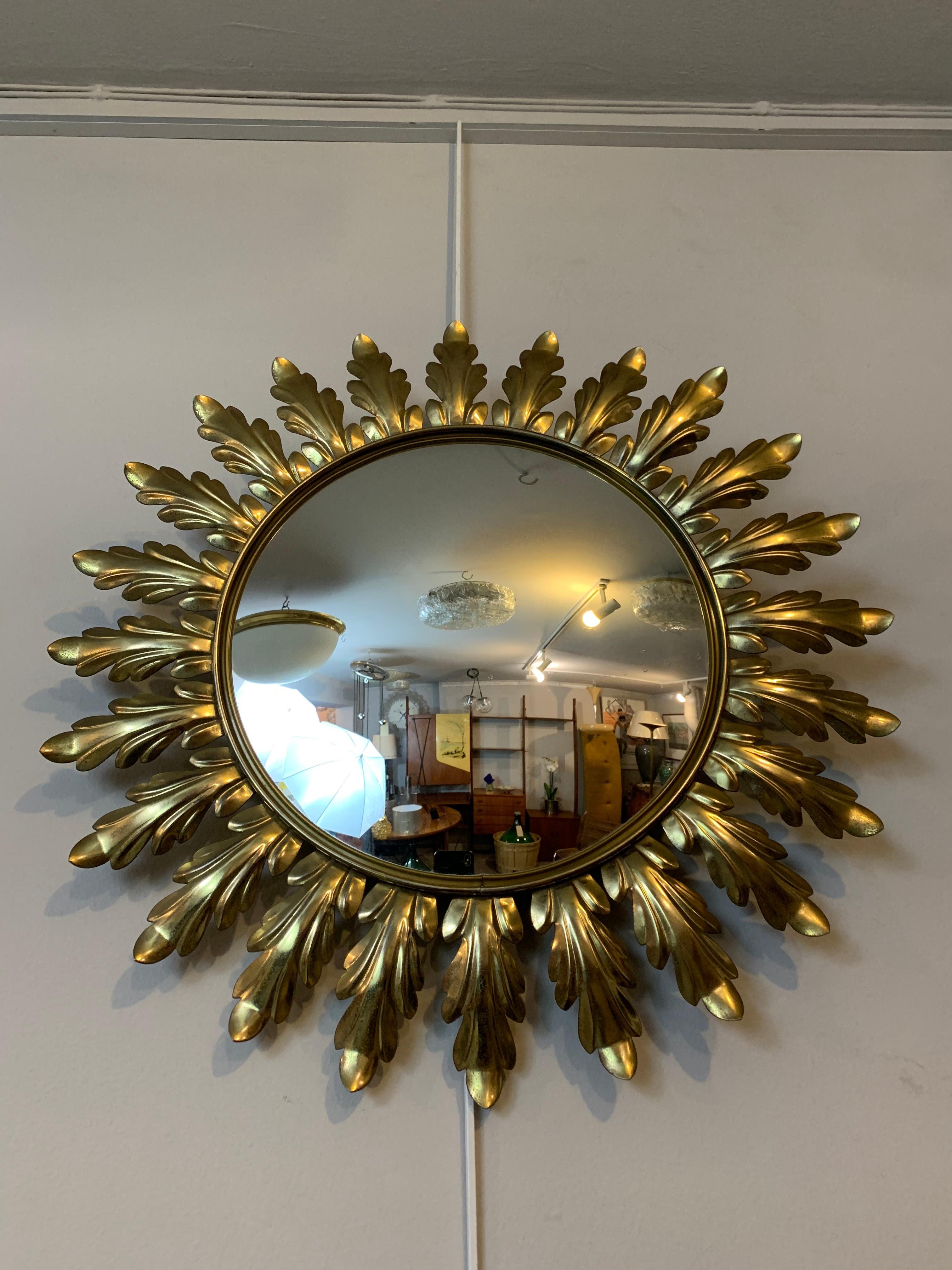 A vintage round wall mirror made in Belgium by Deknudt, circa 1950s. Made with patinated brass leaves which surround the clear glass mirror. The mirror is mounted on a wood backing, covered in aged felt to protect the wall from being scratched. The