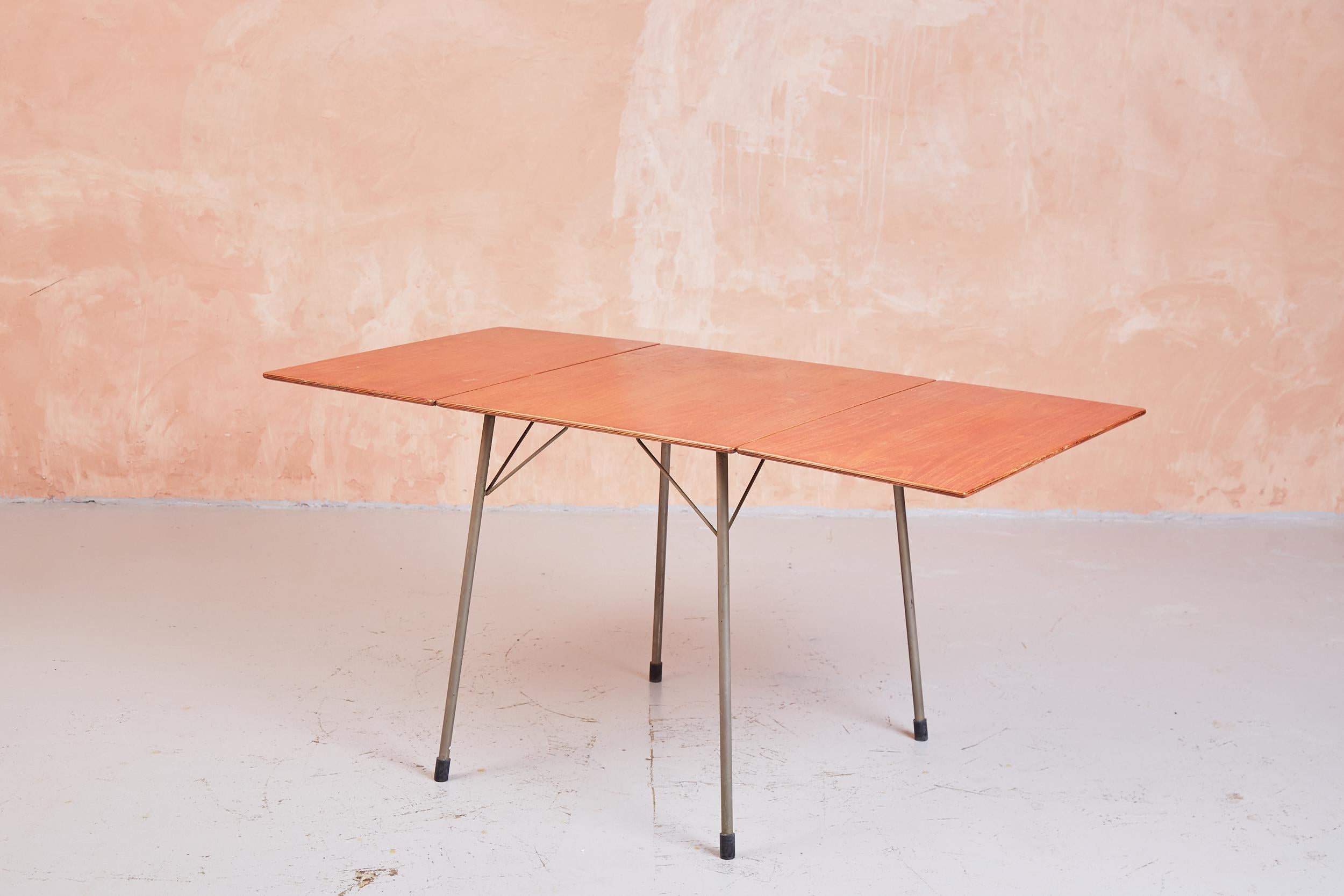 L'un des designs les plus utilitaires d'Arne Jacobsen dans les années 1950, la table 3601 repose sur des pieds en aluminium avec des viroles en caoutchouc, avec un plateau en contreplaqué plaqué teck. Un design simple, presque industriel, qui allie