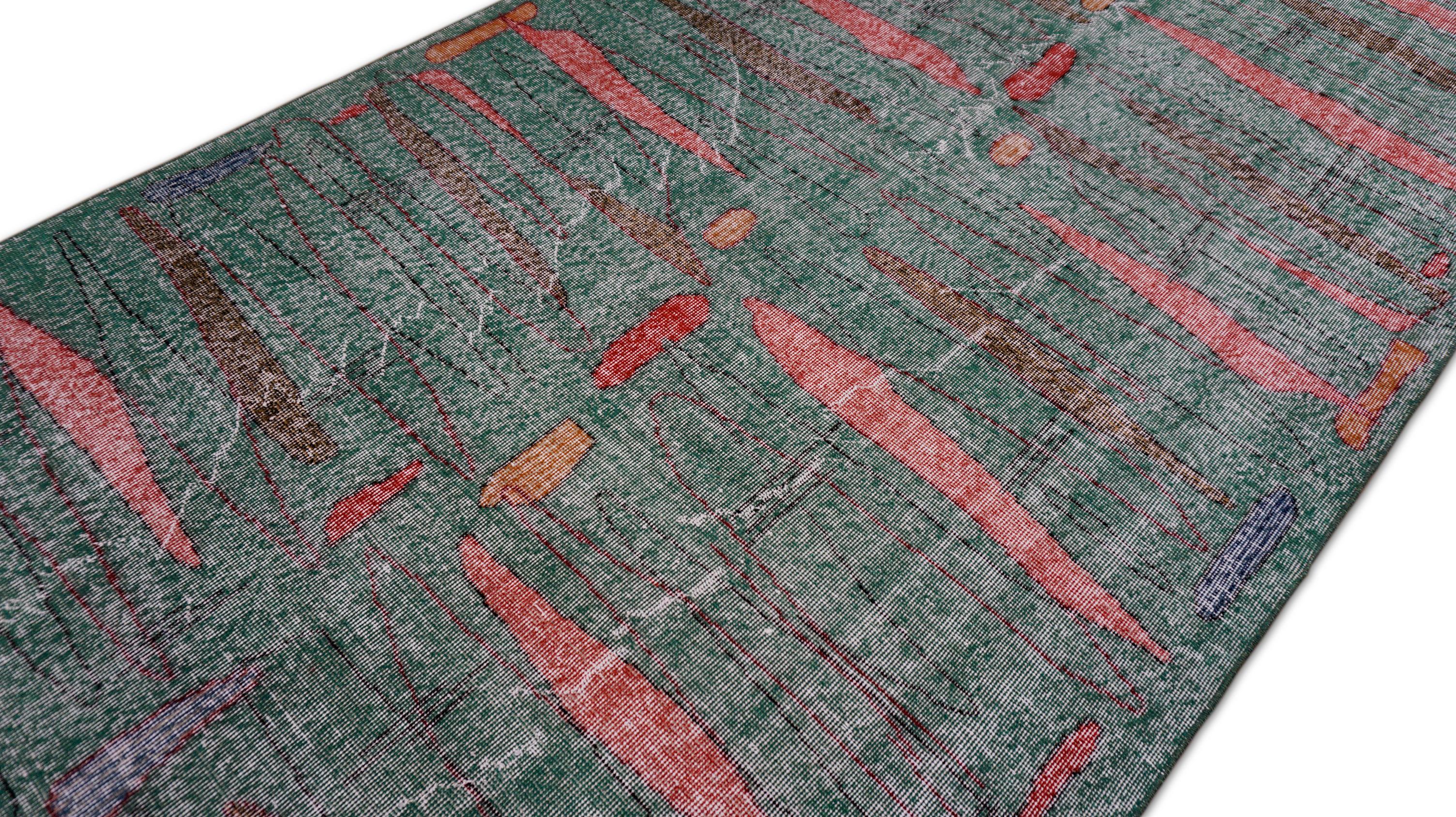 This hand-knotted wool rug is a striking example of modern textile artistry, balancing organic abstraction with minimal color sophistication. Set against a desaturated green ground, the rug features floating, elongated pink, red, gray and brown