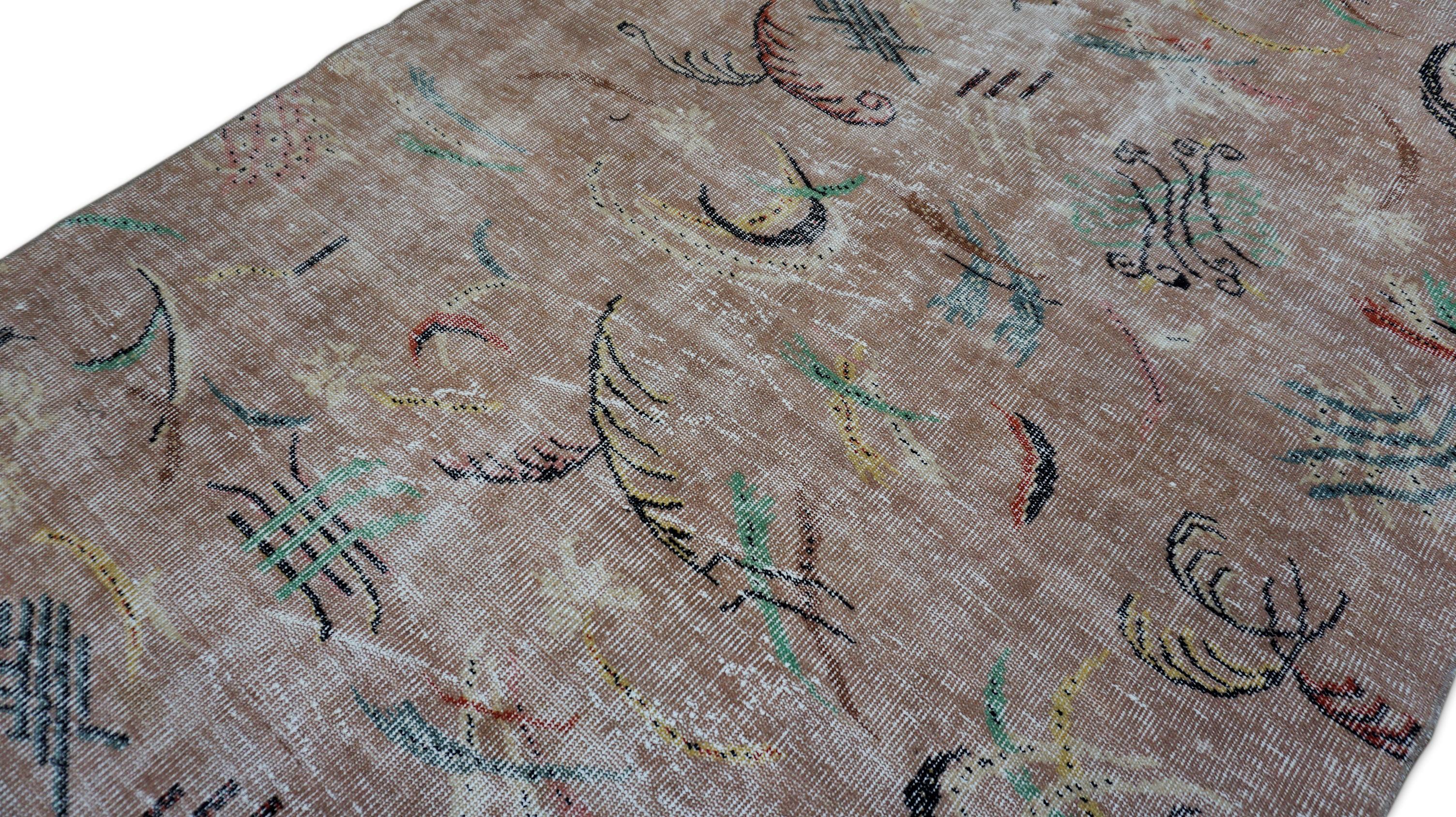This hand-knotted wool rug embodies the harmony between traditional craftsmanship and modern abstract expression. Rendered in a soft brown ground, the design features a scattered array of whimsical, calligraphic motifs in black, and green—evoking