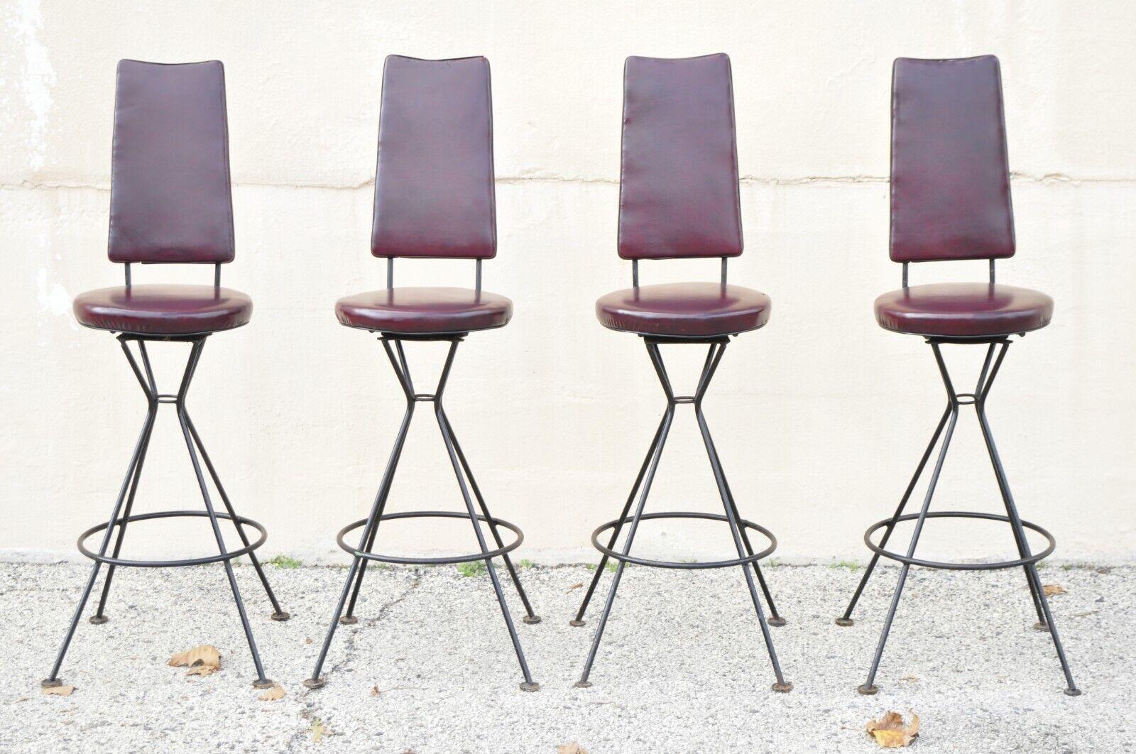 Vintage mid-century atomic era wrought iron burgundy vinyl swivel bar stools - set of 4. Item features a set of (4), wrought iron base, swivel seat with burgundy vinyl round footrest, upholstered back, very nice vintage set, clean modernist lines,