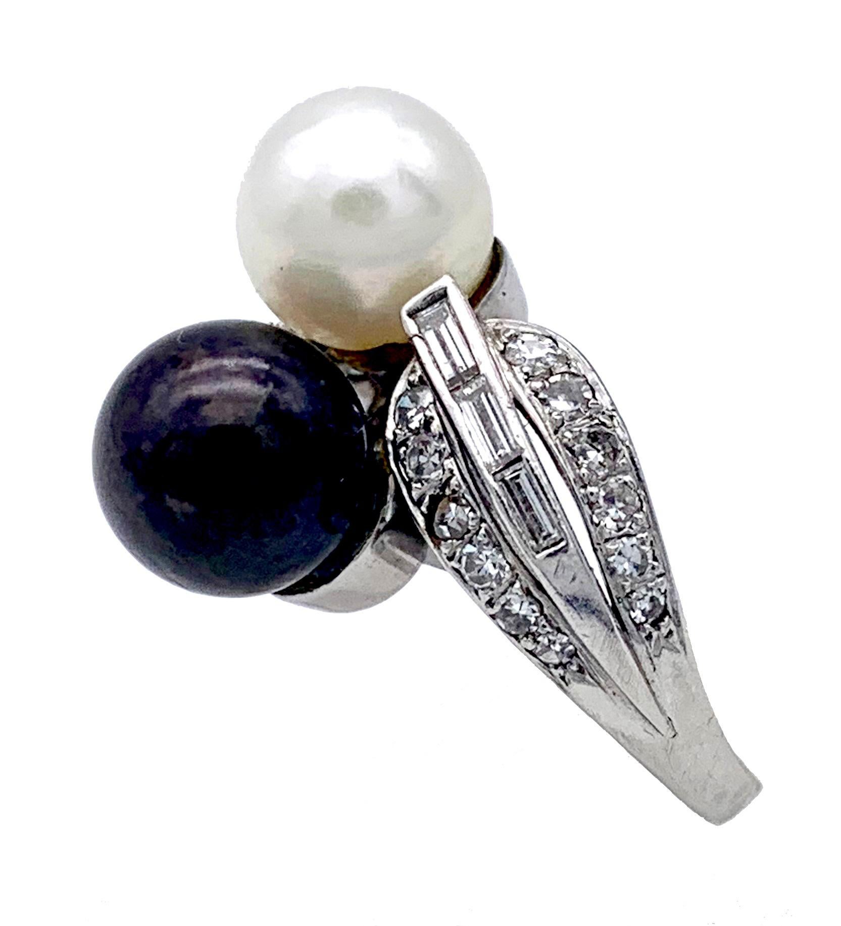 Bei diesem elegant gestalteten Toi & Moi Ring umarmen sich eine braune und eine weiße Zuchtperle. Das Mowments der Perlen wird durch die dynamischen Reihen von Baguette-Diamanten verstärkt. Der Ring wurde ca. 1950 hergestellt. 