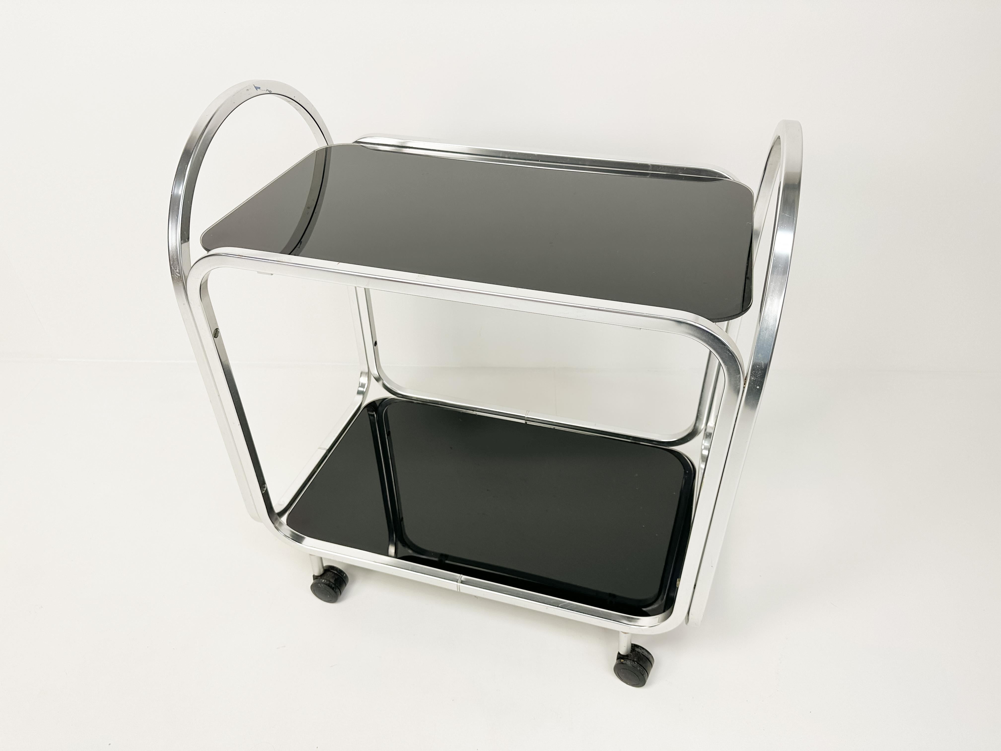 Precioso carrito de servir de mediados de siglo con estantes de cristal negro. El carrito está en general en buen estado vintage, con algunos signos de desgaste y de la edad, algunos arañazos e imperfecciones en la base y en el cristal. 
