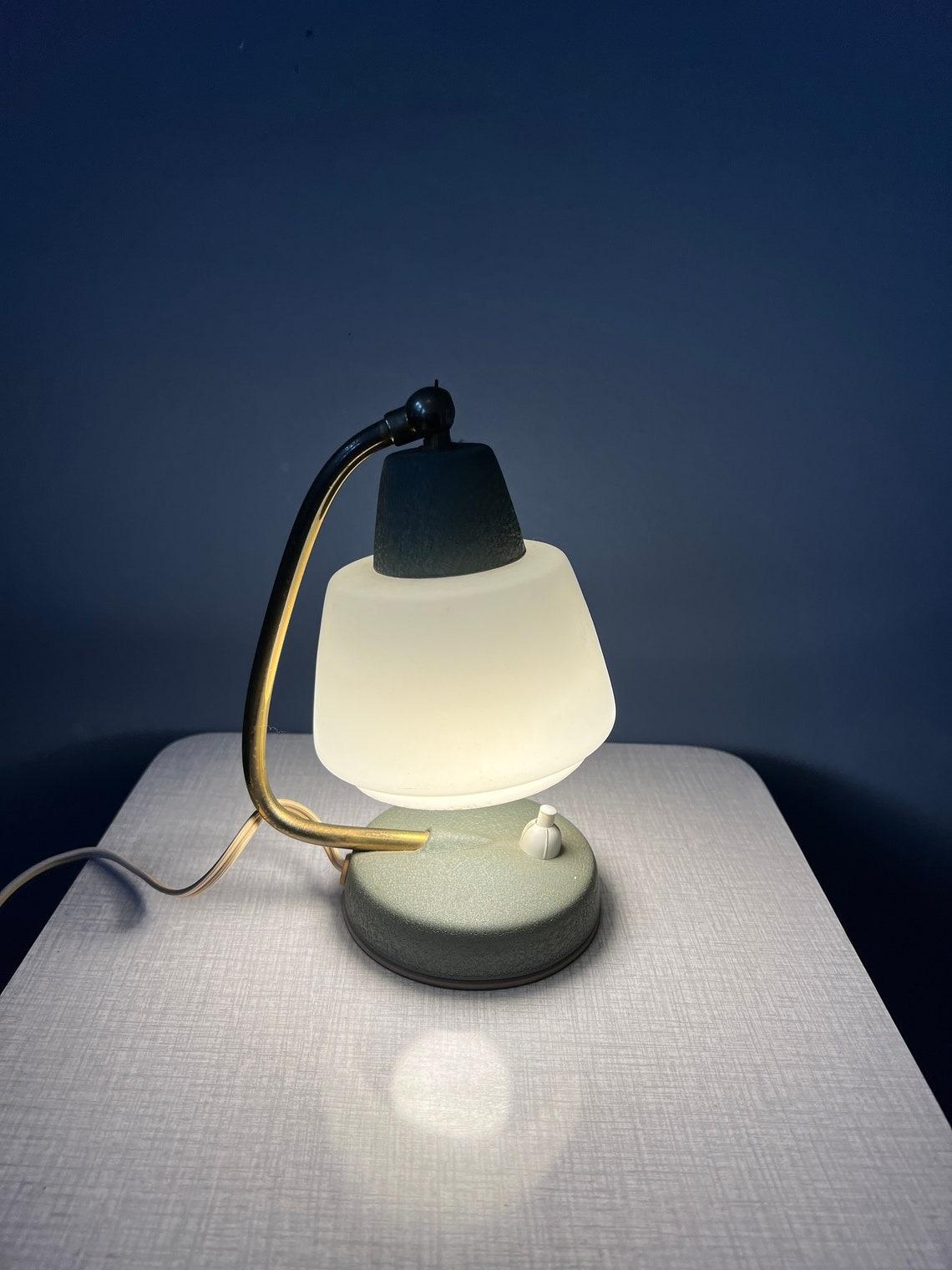 Small vintage mid century bedside table lamp with glass shade. The position of the shade can easily be adjusted, see pictures. The lamp requires an E14 lightbulb and currently has an EU-plug.

Additional information:
Materials: Glass, metal
Period: