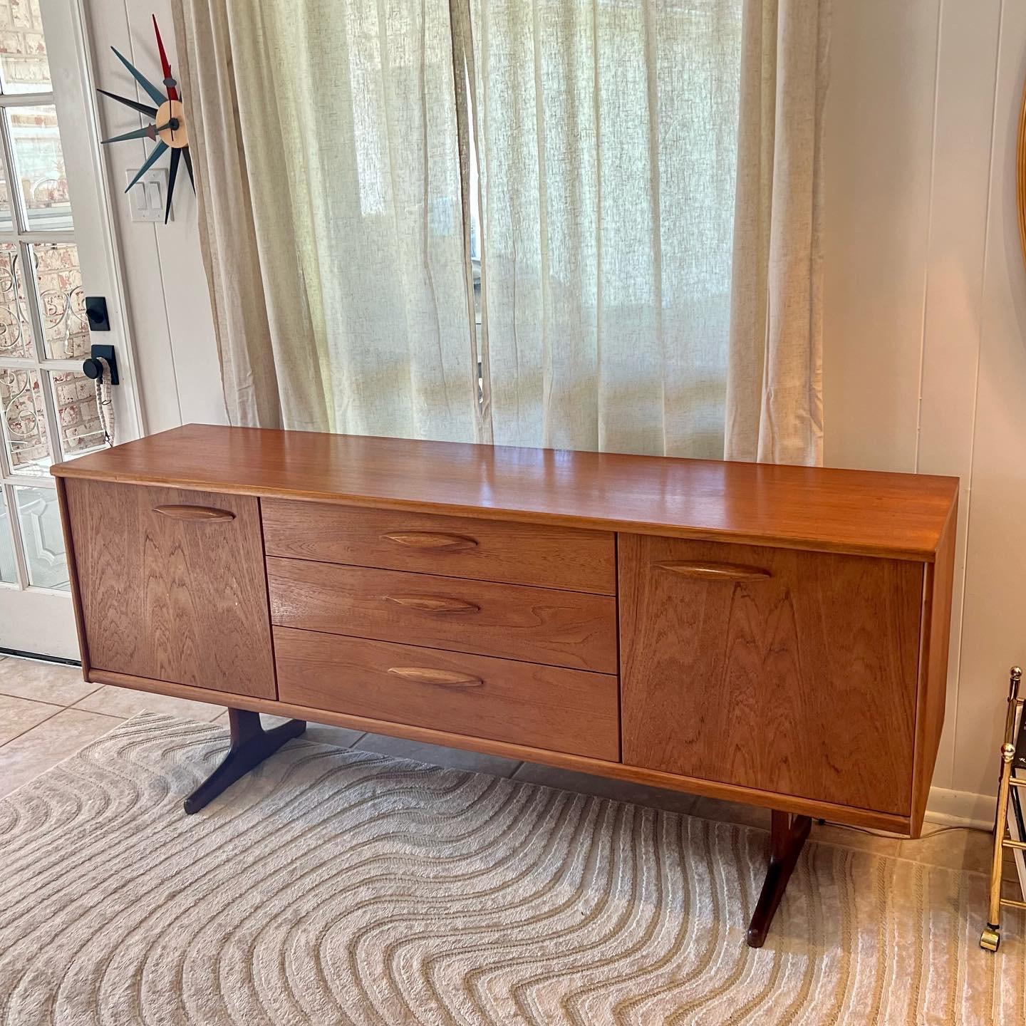 Mid century british teak sideboard by Frank Guille for Austinsuite. Featuring simplistic Scandinavian influenced design with stylish handles and trapeze style base. The teak has a nice vintage golden patina that only age can achieve. Overall in