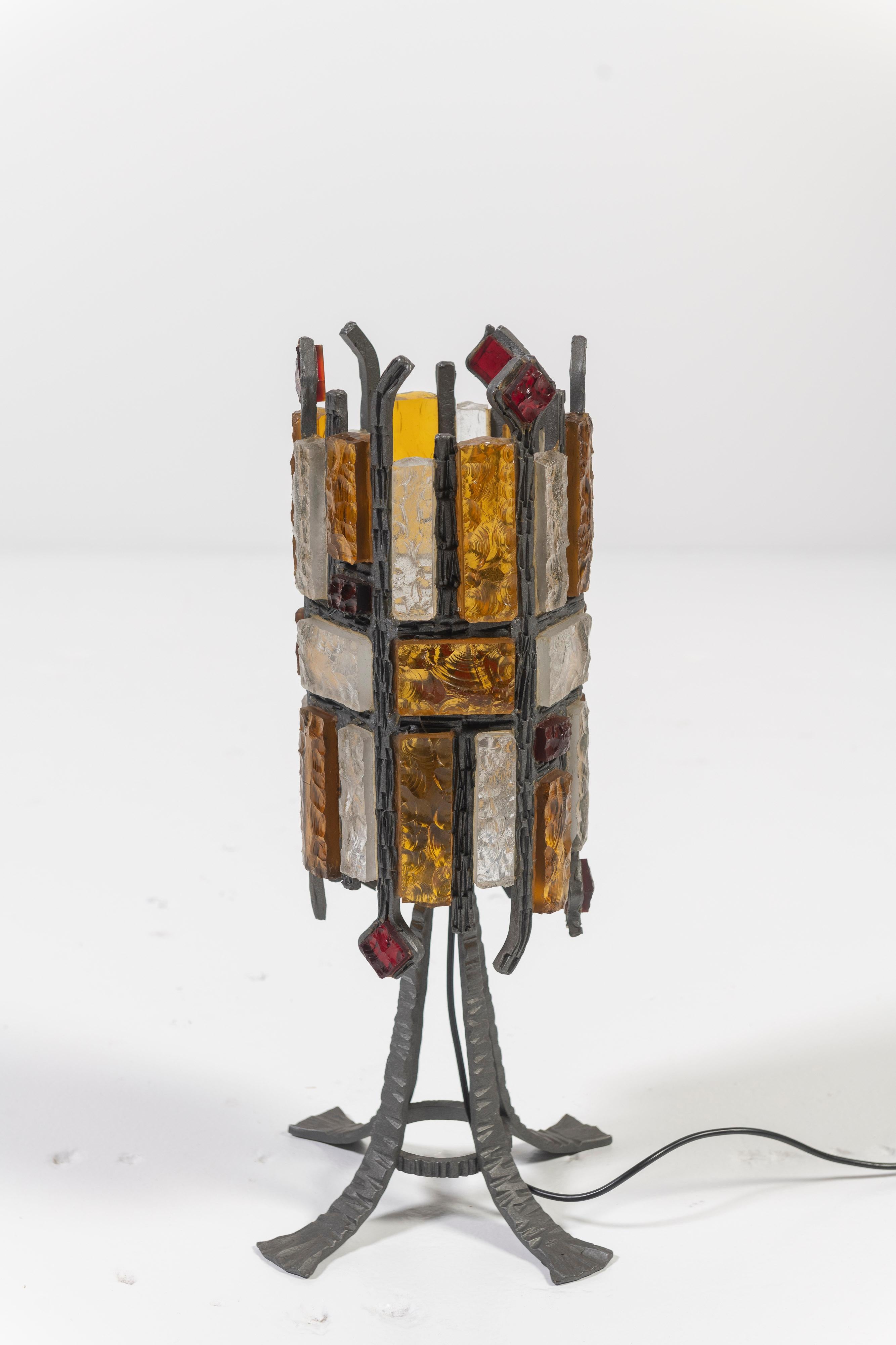 Lampe de table brutaliste unique, avec des matériaux bruts et texturés, une silhouette trapue et toutes les couleurs d'une flamme, rouge, ambre et ivoire - parfaite pour apporter un peu de mystère et de chaleur à un endroit spécial dans n'importe