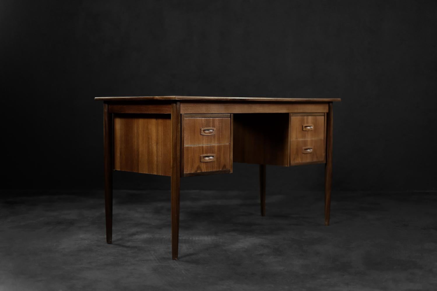 This classic desk was made in Denmark during the 1960s. It was finished of teak wood in a warm shade of brown, with visible grain detail. The desk has four drawers. Two on both sides. The slender and tall legs of the desk are made of wood. This