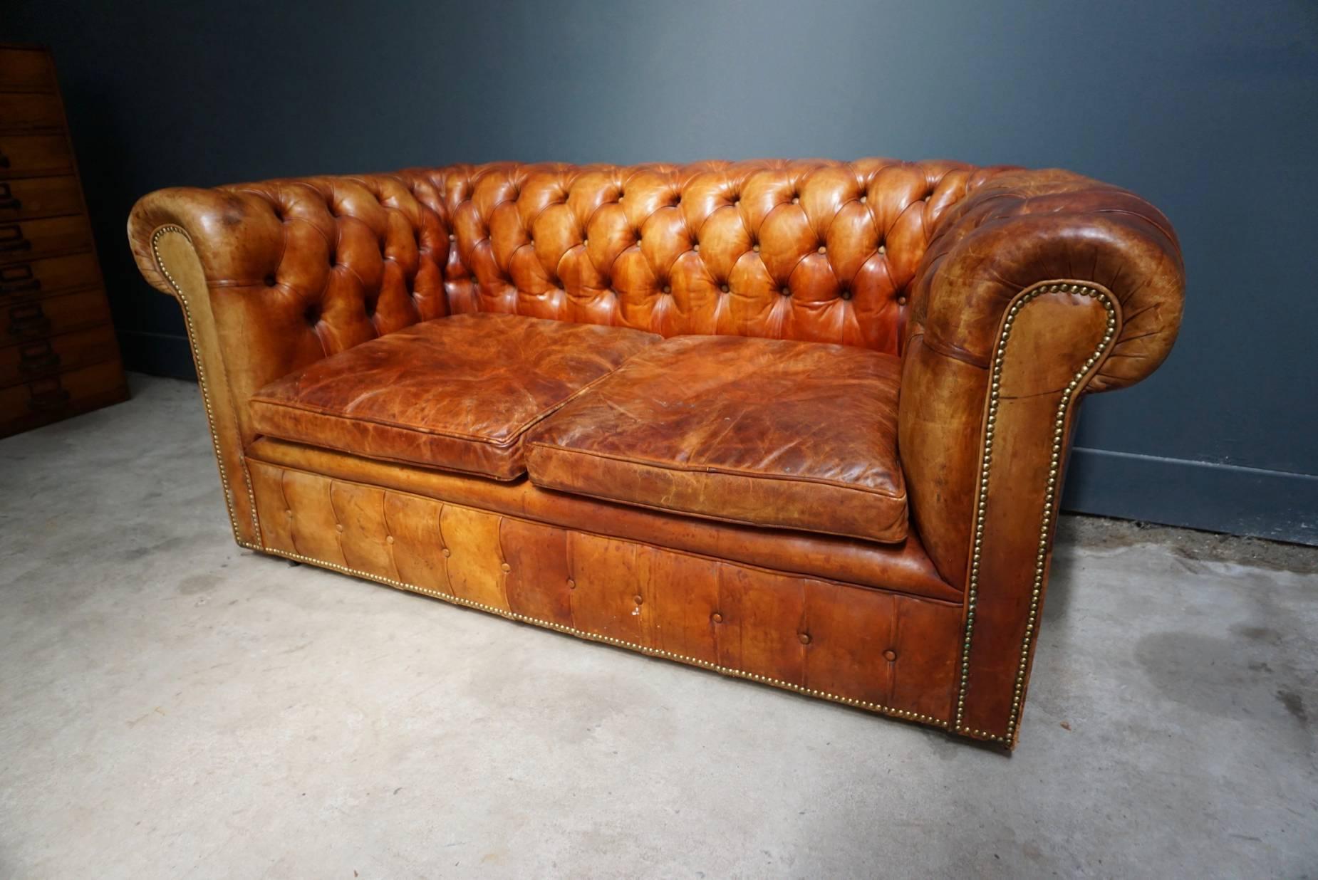 This vintage Chesterfield sofa was handmade in England, circa 1950-1960. The piece is upholstered in hand dyed cognac brown leather. The Chesterfield features loose cushions. It remains in a good vintage condition and retained a rich patina over the