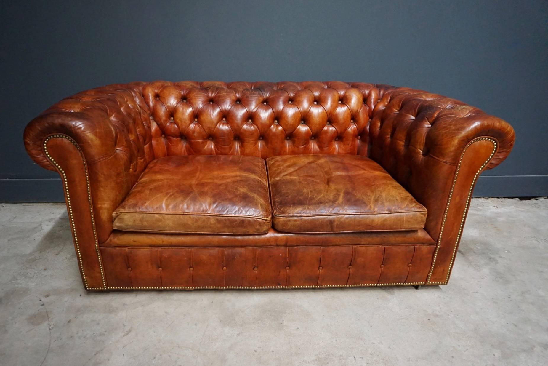 This vintage Chesterfield sofa was handmade in England, circa 1950-1960. The piece is upholstered in hand dyed cognac brown leather. The Chesterfield features loose cushions. It remains in a good vintage condition and retained a rich patina over the