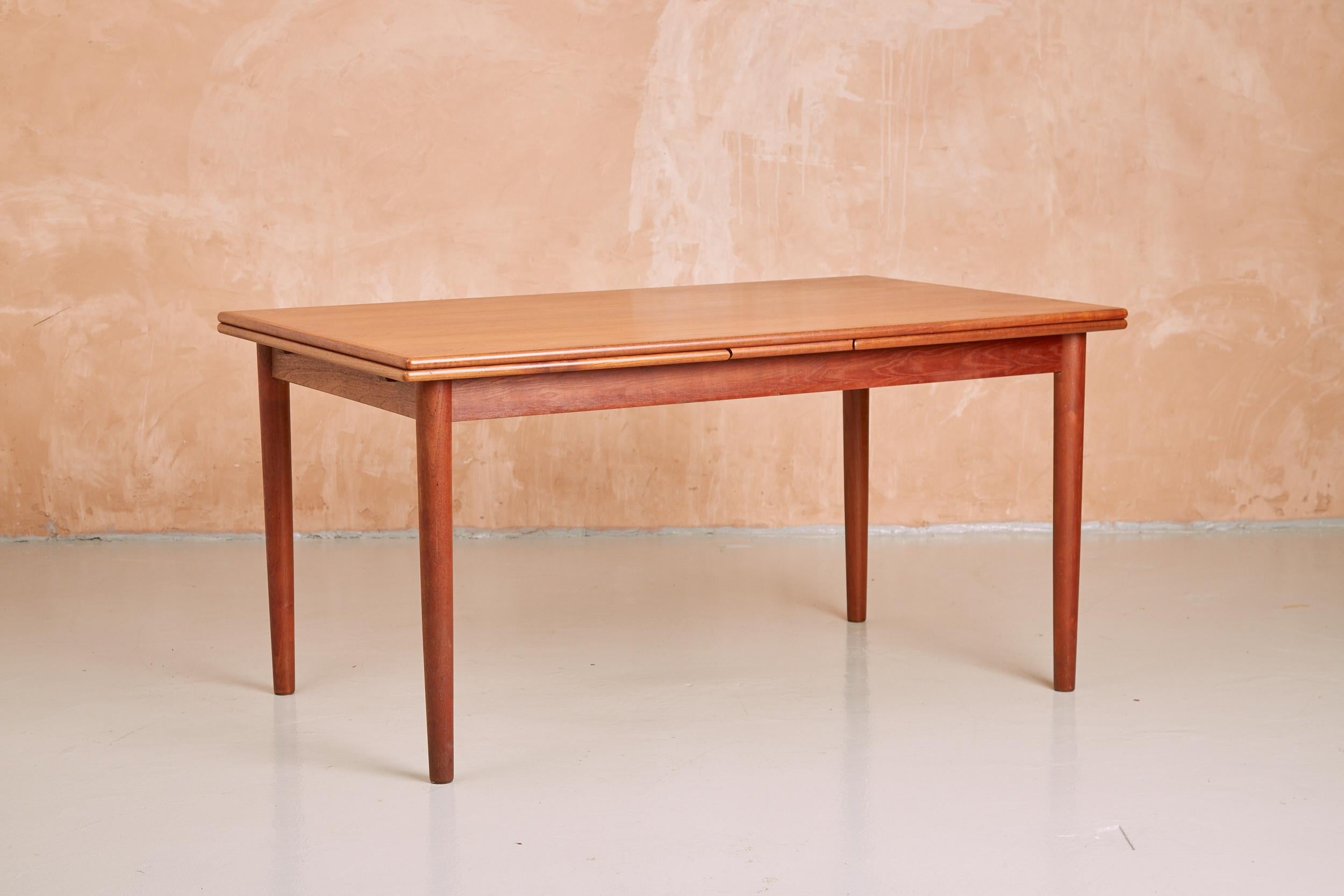 An iconic draw leaf teak extending dining table, manufactured by the Danish brand AM Møbler (Ansager Møbler) in the 1960s.

Seats 6 when closed (145 cm) and up to 10 when extended (266 cm). The leaves extend simply by pulling out from below the main