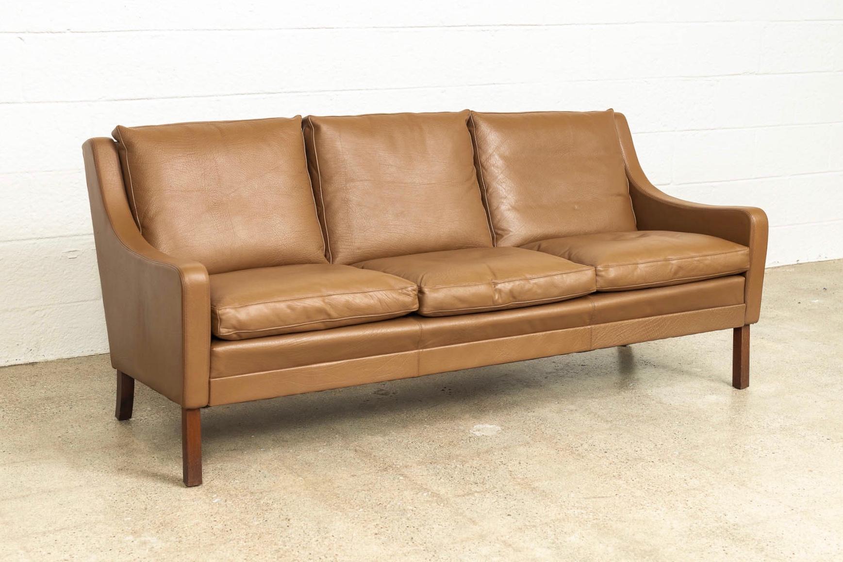 This vintage midcentury Danish modern leather sofa in the style of Borge Mogensen was made in Denmark circa 1960. With classic Danish styling, it features clean lines and gentle curves. This three-seat couch has six removable zippered cushions and