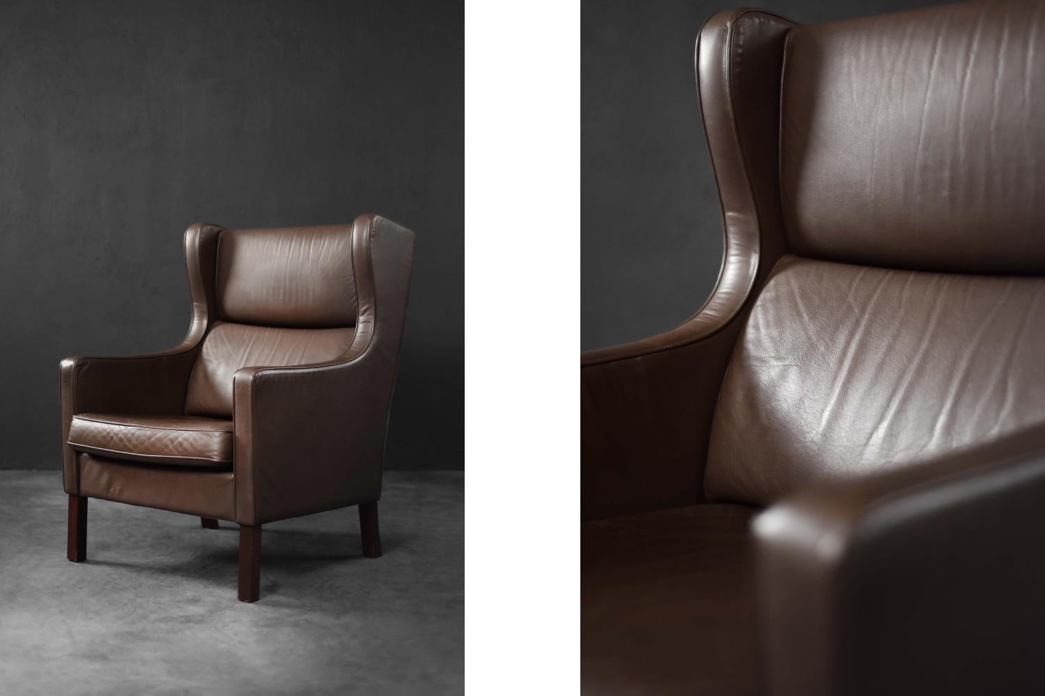 Questa classica sedia ad ala modernista è stata prodotta in Danimarca negli anni Sessanta. Rivestita interamente in pelle naturale color cioccolato scuro, il design della sedia si basa su linee semplici, visibili sul davanti. La struttura laterale