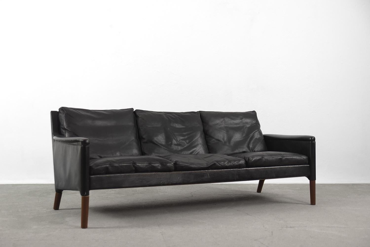 Dieses dreisitzige Ledersofa wurde in den 1950er Jahren von Kurt Østervig für den dänischen Hersteller Centrum Møbler entworfen. Es handelt sich um das Modell 55 aus der frühen Produktionszeit. Das Sofa ist mit schwarzem Leder mit natürlicher Patina