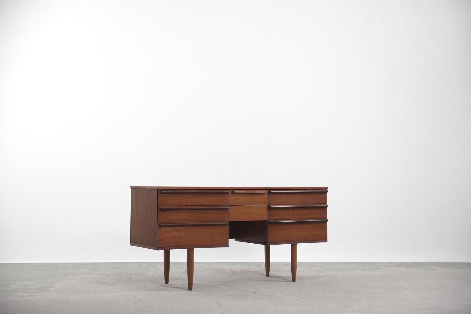 This classic desk or dressing table was probably manufacturer by English maker Avalon, which produced Danish design furniture. This piece was created during the 1960s. The desk has an elegant look. It has six larger drawers and two smaller ones in
