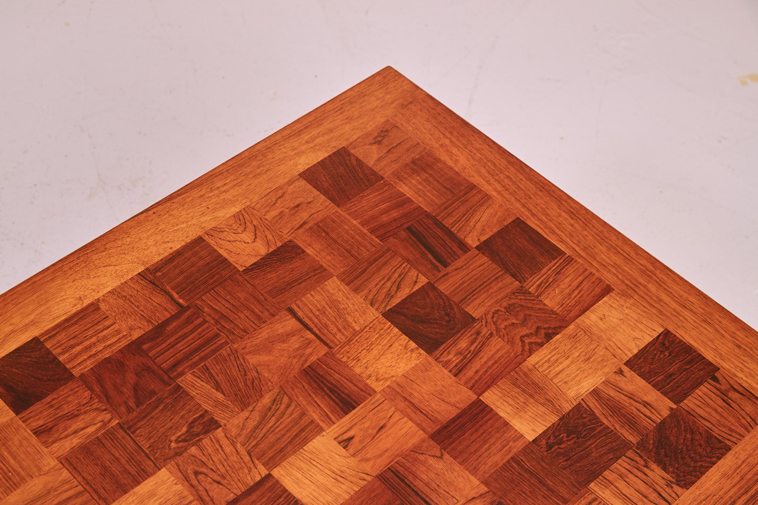 A classic Cado coffee table finished in rosewood with an elegant checkerboard design top with a beautiful mixed grain. The top has a lacquer finish making it extremely durable and water resistant. The coffee table sits on bold square sleigh legs for