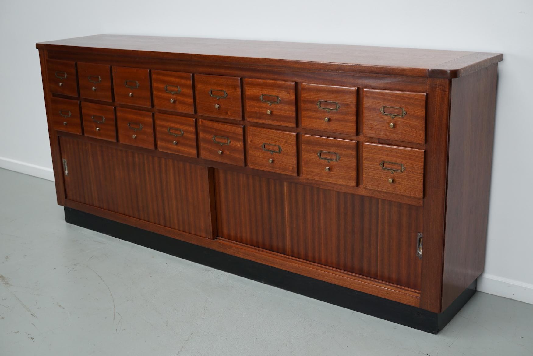 Questo mobile è stato prodotto negli anni 1950/60 nei Paesi Bassi. Dispone di 16 cassetti in legno duro di qualità e di due grandi ante scorrevoli. Le dimensioni interne dei cassetti sono: DWH 31,5 x 18,5 x 13 cm. 