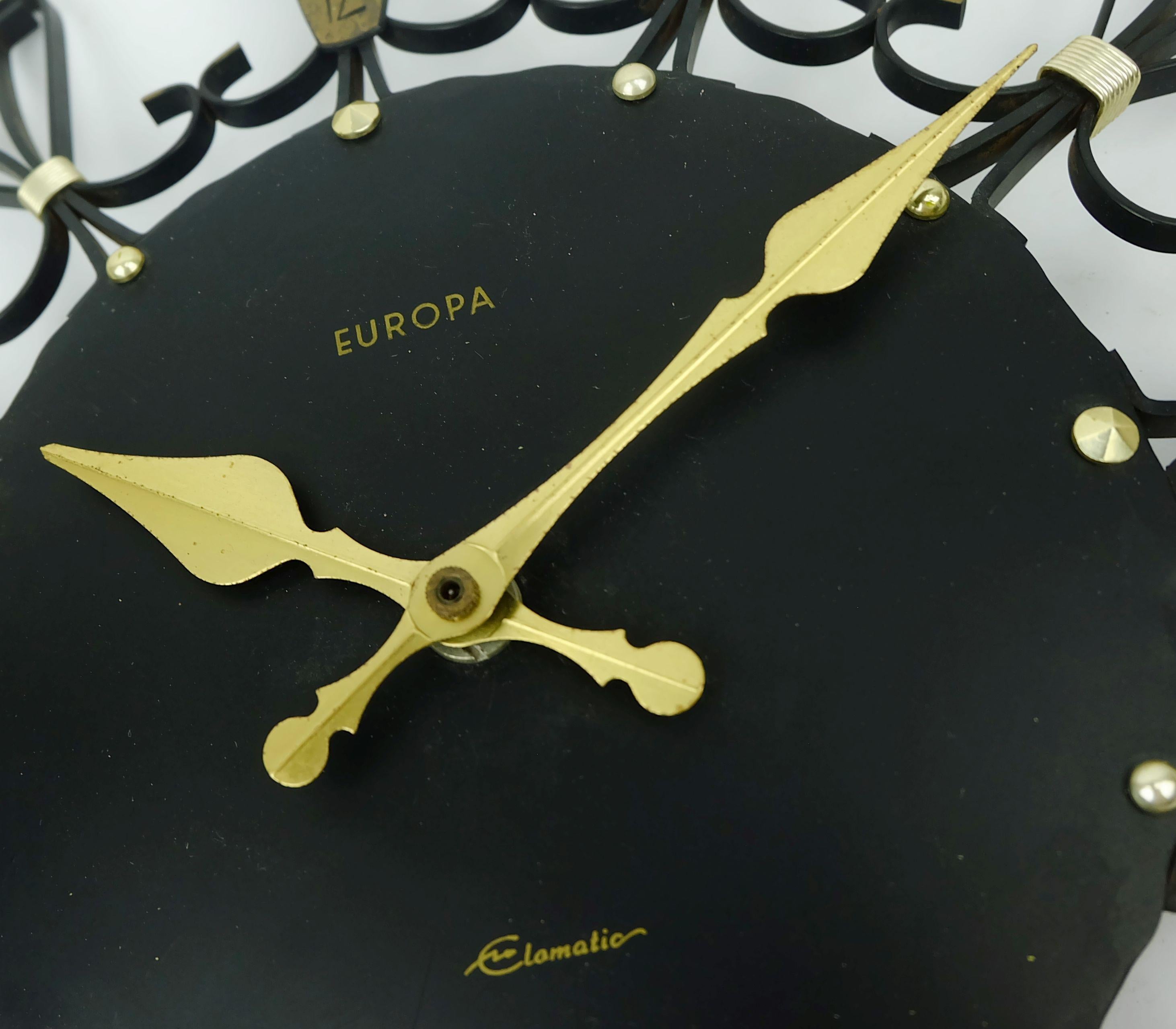 Wanduhr aus der Mitte der 1960er Jahre, hergestellt von Europa Elomatic. Funktioniert mit Batteriebetrieb (Batterie ist nicht enthalten). Hergestellt aus mattschwarzem Metall und Messing.

Abmessungen: Durchmesser 12 1/2