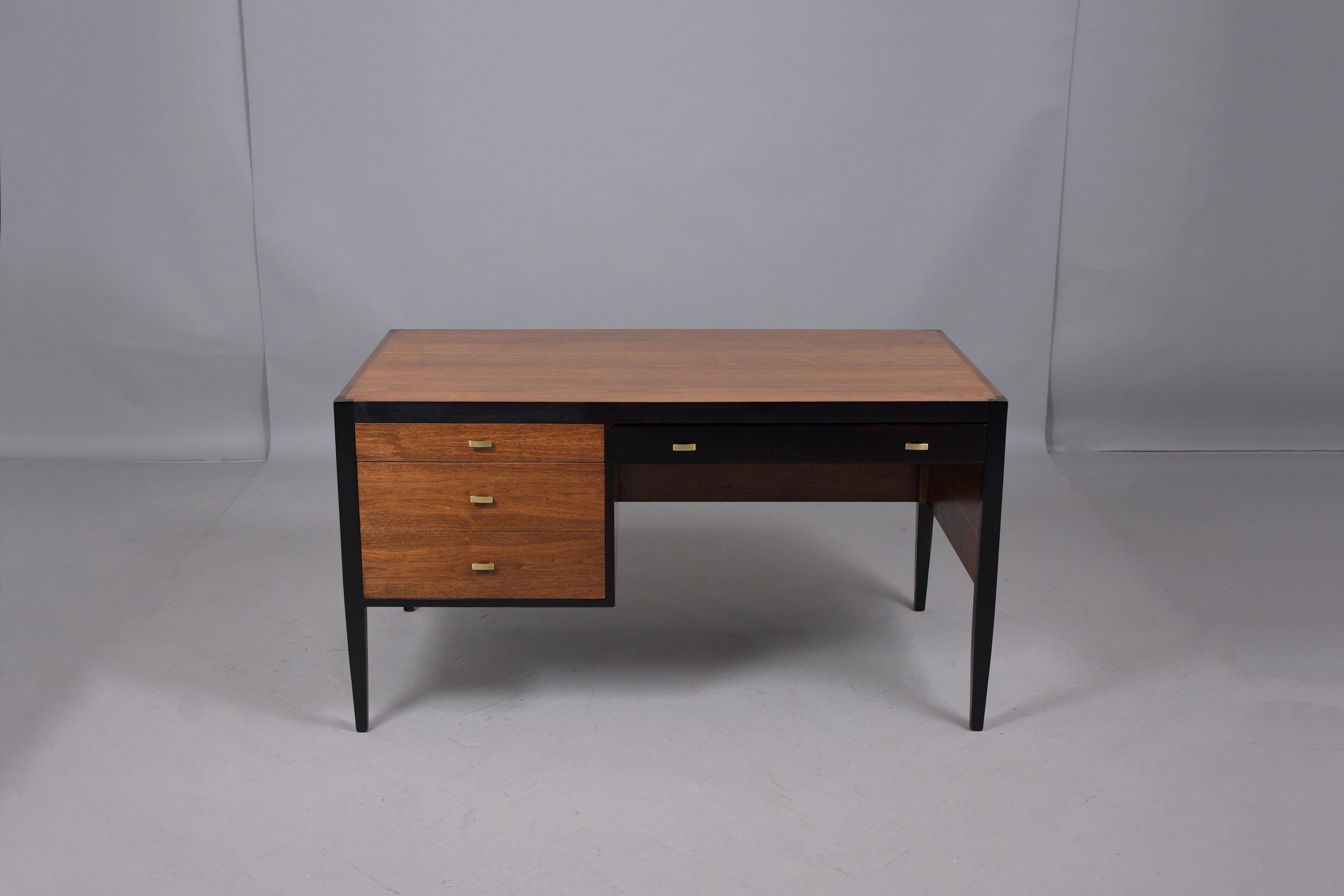 This sleek vintage mid-century modern desk has been professionally restored and features a newly stained walnut and ebonized color combination with a semi-gloss lacquered finish. The desk comes with three drawers with brass pulls that all open with