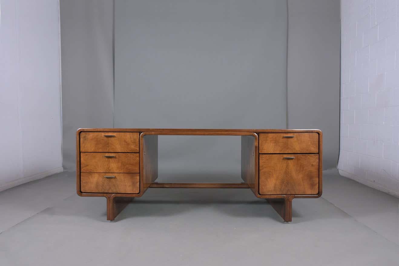 An extraordinary Mid-Century Modern desk hand-crated out of walnut wood newly stained a rich walnut color with a lacquered finish and professionally restored by our team of craftsmen. The desk features a large rectangular top with curved edges is