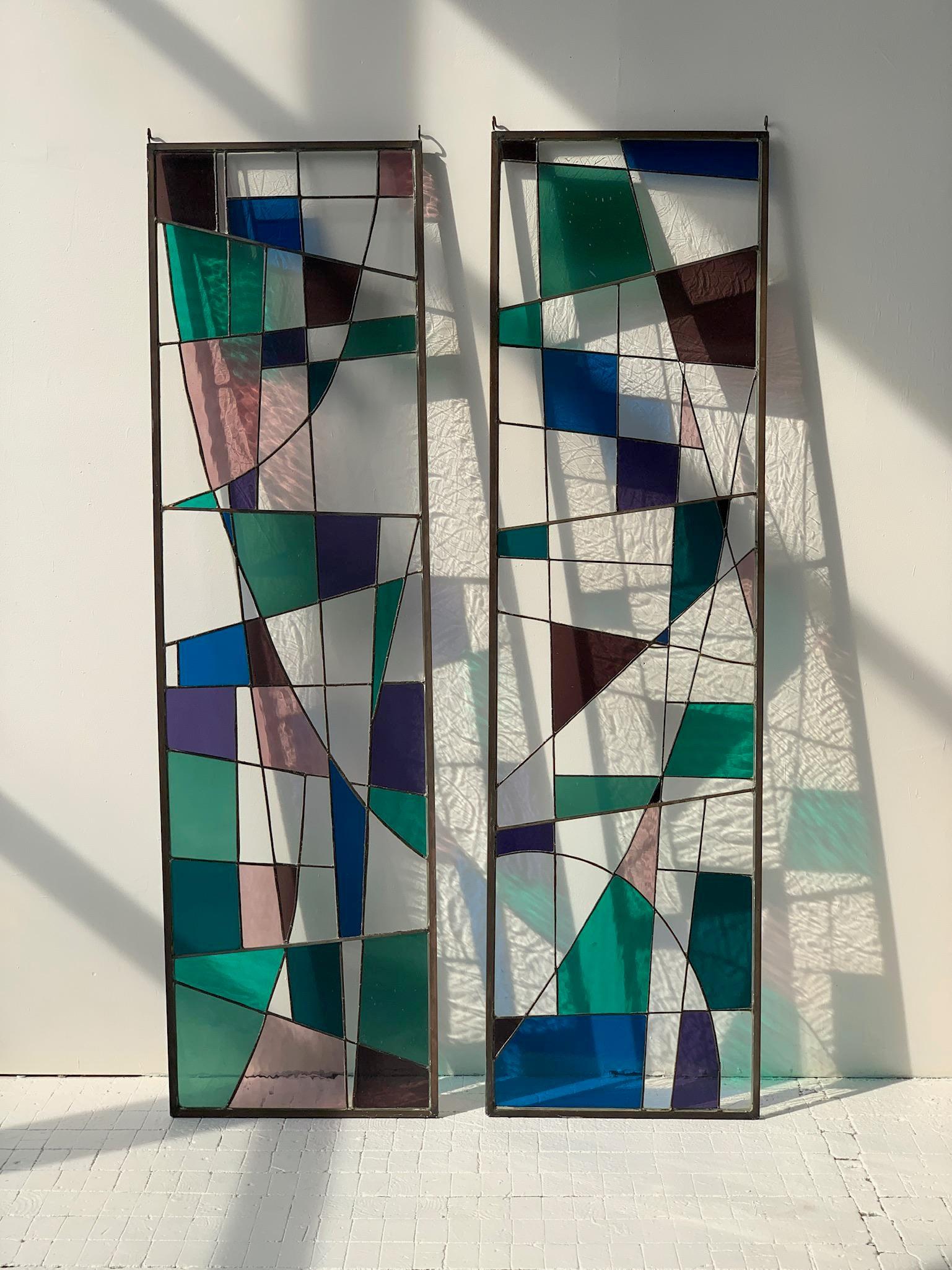 Vintage Mid Century Geometric Abstract Stained Glass Panels, A Pair, Circa 1960s. Asymmetrical mosaic of stained glass rendered in hues of blue, purple, green and clear. The various shapes of glass are expertly crafted and leaded together to create