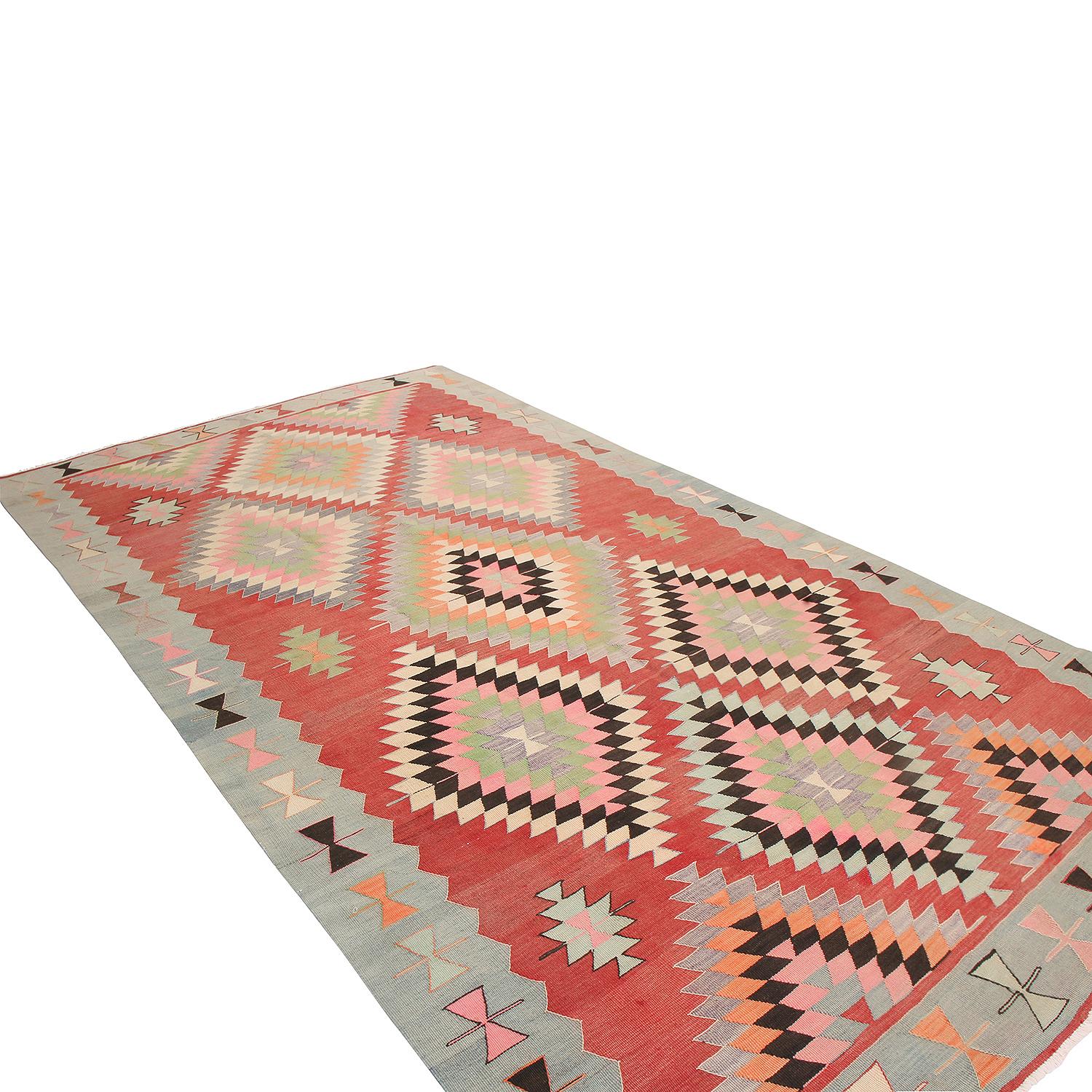 Flat-woven by hand in high-quality wool originating from Turkey between 1940-1950, this vintage Kilim rug enjoys a rare teal border background and complementary red field background, both tastefully abrashed and accented by the rare pagination of