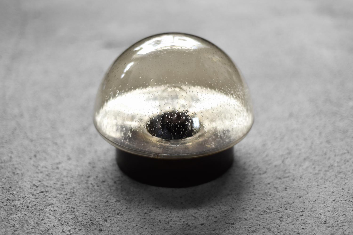 La lampada da soffitto o applique decorativa è stata prodotta in Germania negli anni '60. Il punto focale della lampada è il paralume in vetro fumé soffiato a mano, pieno di piccole bolle d'aria che creano un effetto luminoso unico. Il bagliore