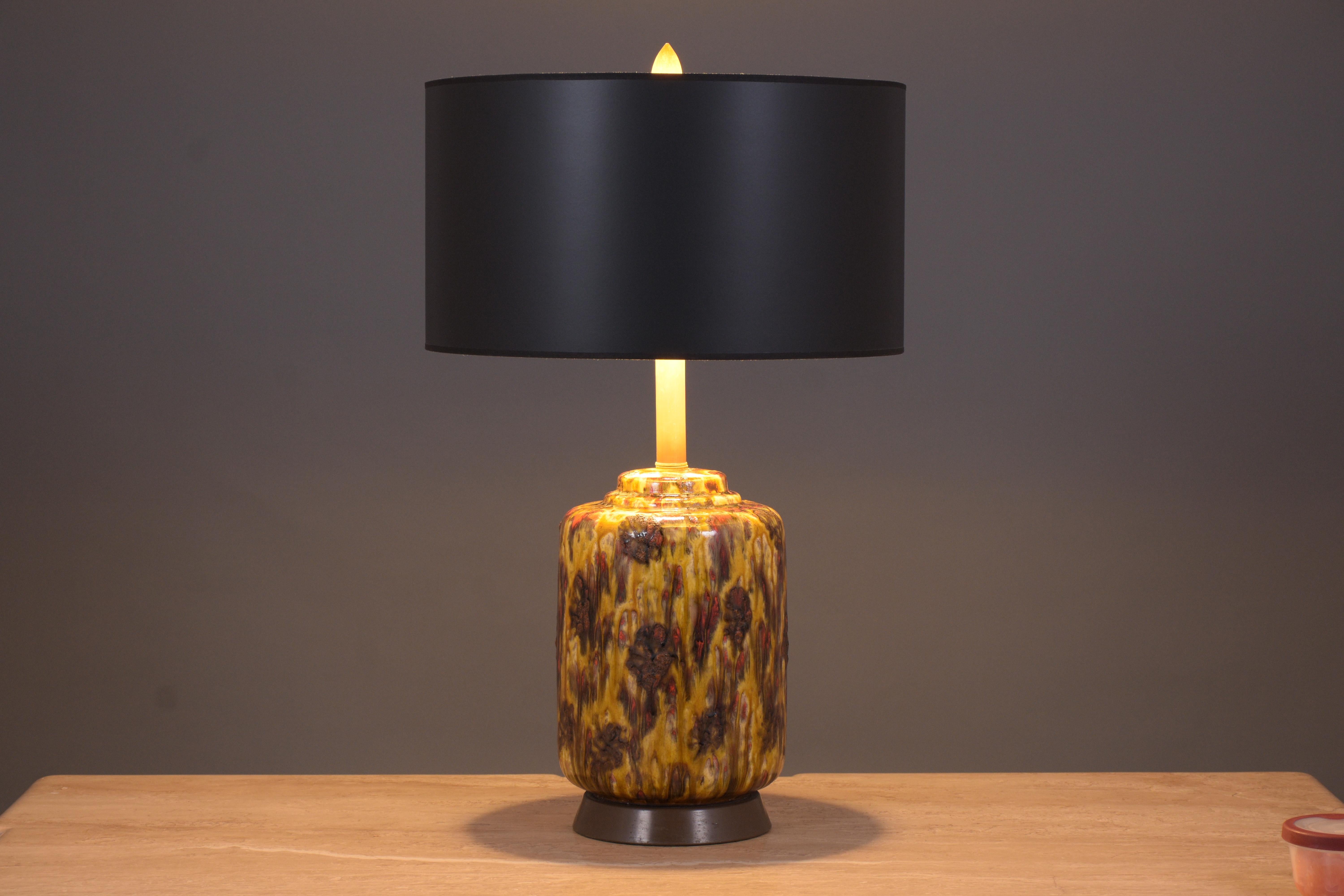 A beautiful mid-century table lamp featuring a cylinder ceramic base with a floral design with a beautiful glaze finish. The lamp comes with a new black shade with a gilt finish, is wired to U.S. standards, and is in working condition. The lamp is