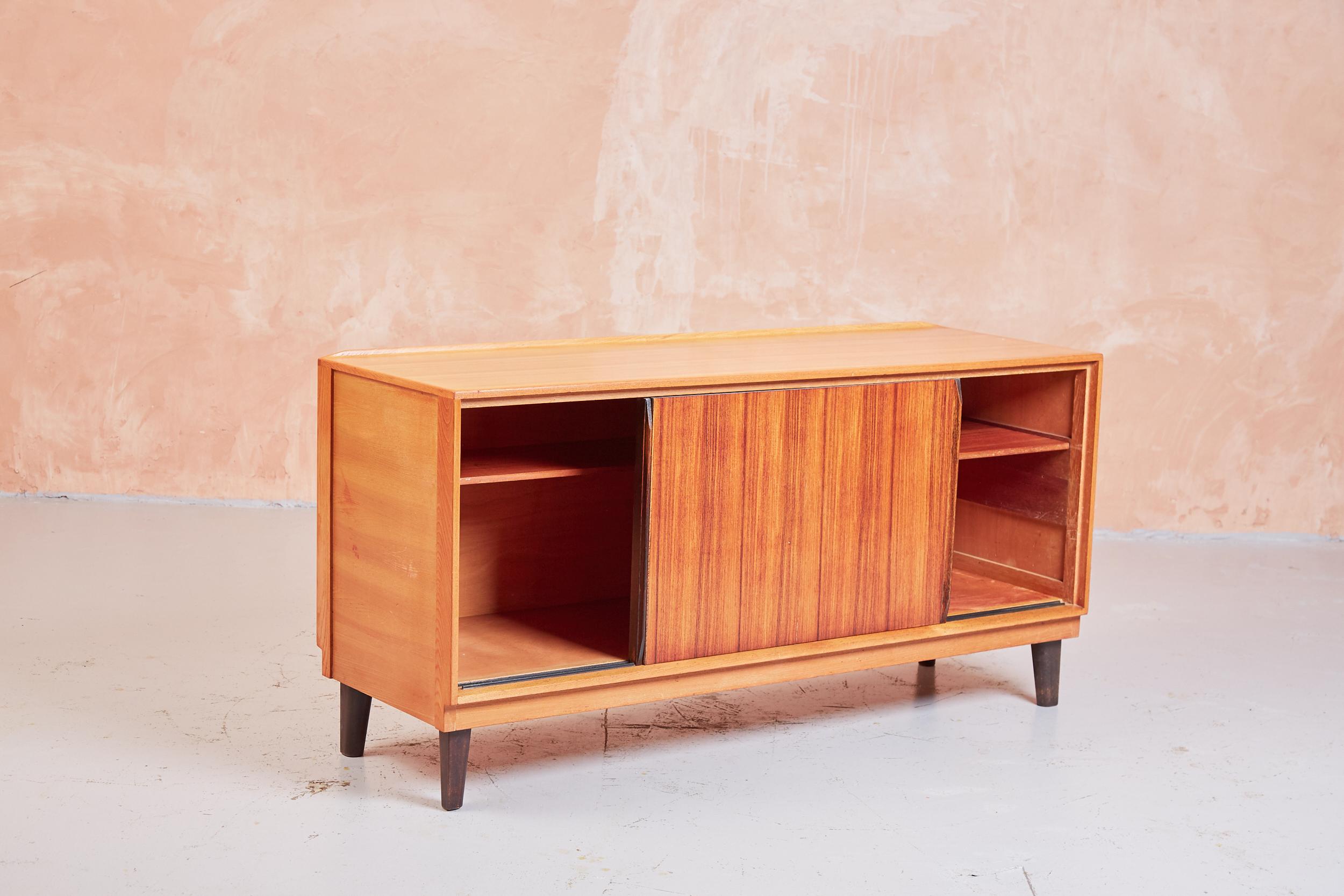 A sleek and sturdy sideboard designed and manufactured by Gordon Russell, originally sold at Heal’s. A rare 1950s mid century classic design, constructed in elm with Indian Rosewood sliding doors. The spacious storage compartments each include a