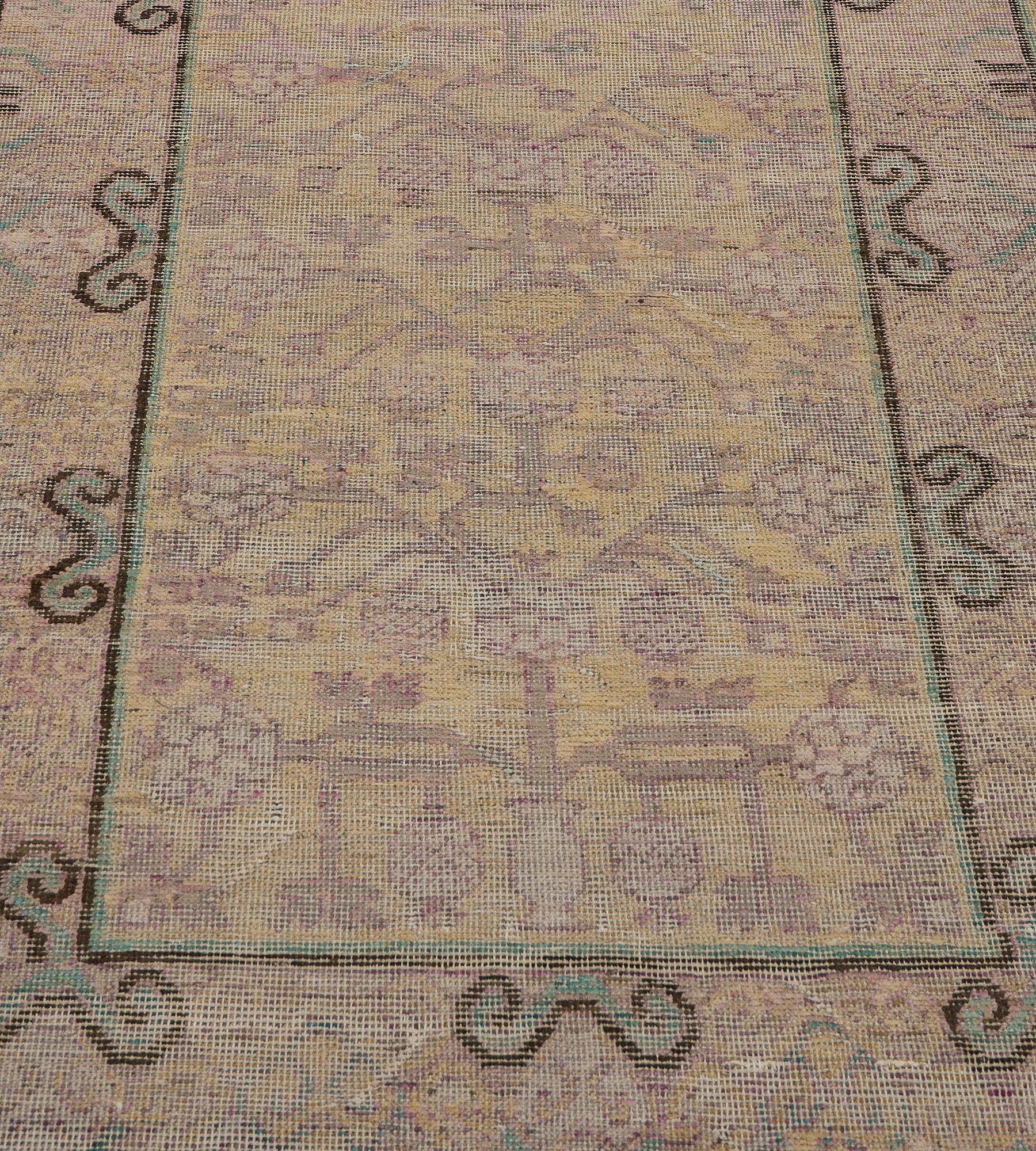 This vintage, circa 1950, Khotan runner has a sandy-yellow field with an overall design of aubergine-purple angular pomegranate vine, in a broad sandy-yellow cloud-motif and dense polychrome linked hooked lozenge vine between charcoal-brown and